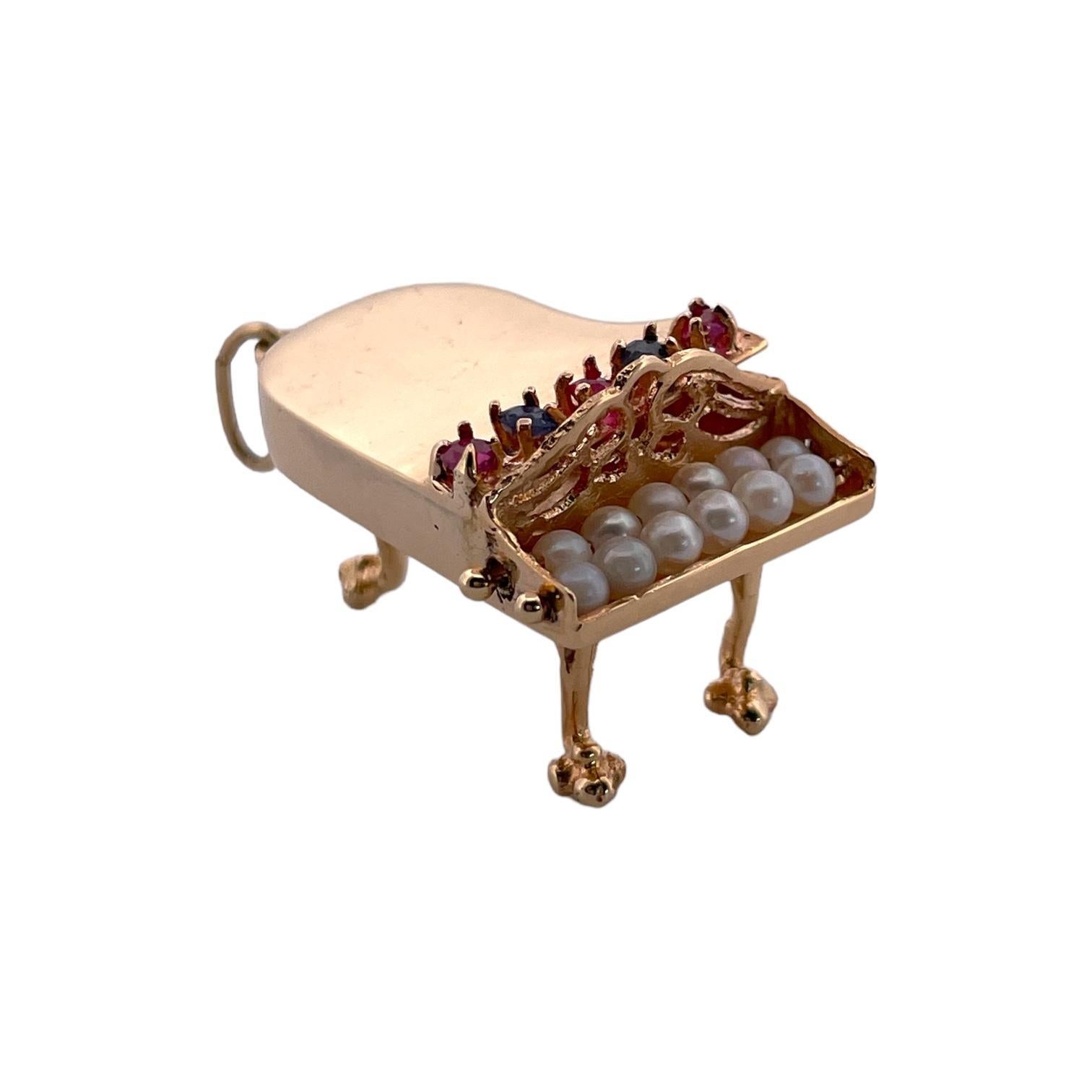 Ce pendentif exquis capture le charme d'un piano à queue dans une forme miniature. Réalisé en or brillant, le pendentif présente un design détaillé avec un couvercle orné de pierres précieuses vibrantes dans des tons bleus et roses. Le clavier est