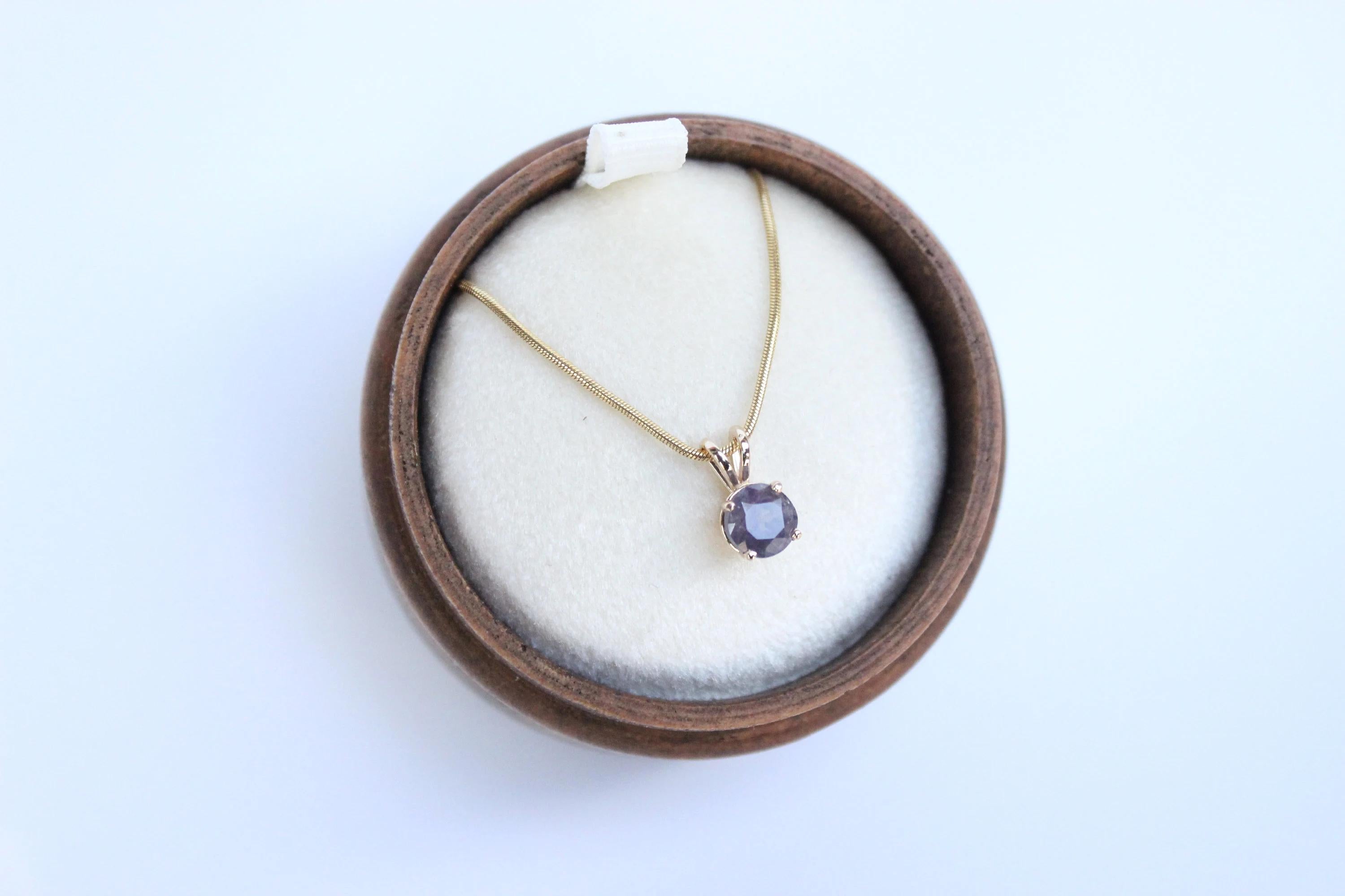 This stylish purple sapphire necklace pendant is a unique and eye-catching piece. The round-cut sapphire weighs approximately 1 carat, showcasing its vibrant color and charm.  

The pendant is paired with a 20-inch, 1mm snake chain in 14k yellow