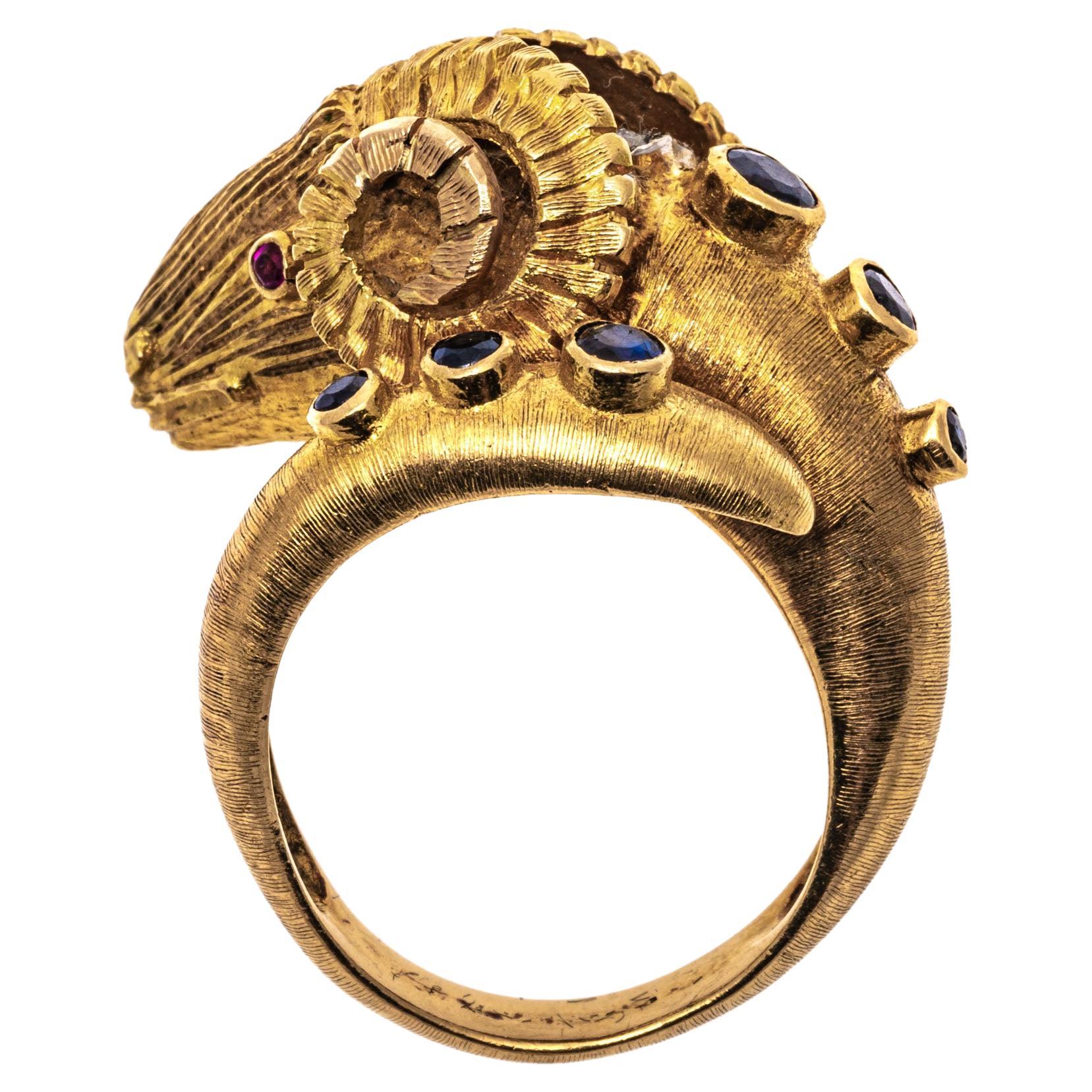 14k yellow gold ring. This imposing crossover ring is a detailed figural ram's head, with ribbed, curved horns, a tooled face, faceted ruby eyes, approximately 0.06 TCW, and a round faceted diamond, approximately 0.015 CTS set behind the head. Set