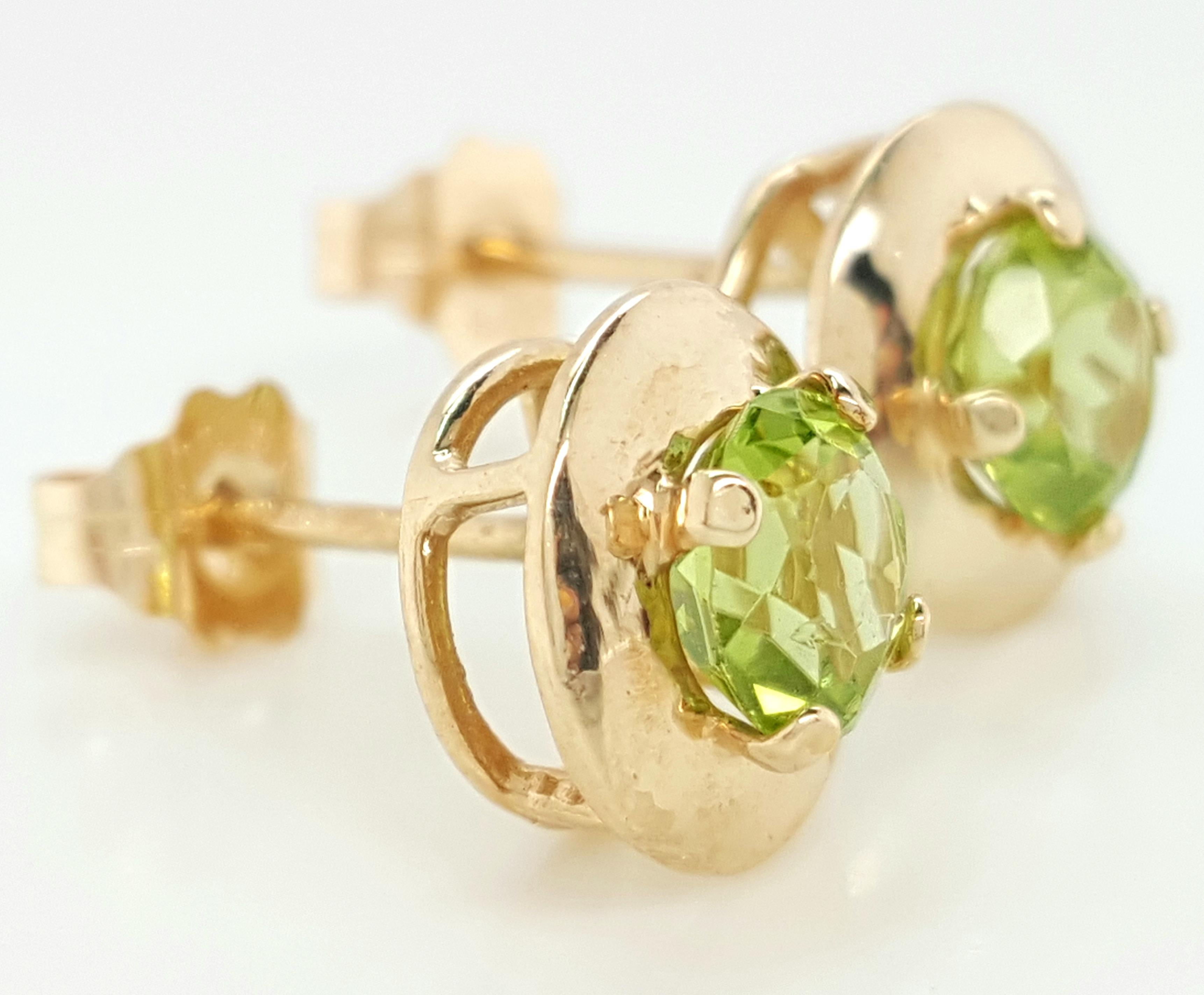 14K Yellow Gold Round Peridot Stud Earrings.  The earrings feature a matched pair of faceted round peridots weighing approximately  0.98 carats.  The peridots are each set into a 14 karat yellow gold four prong setting with a halo of gold, completed