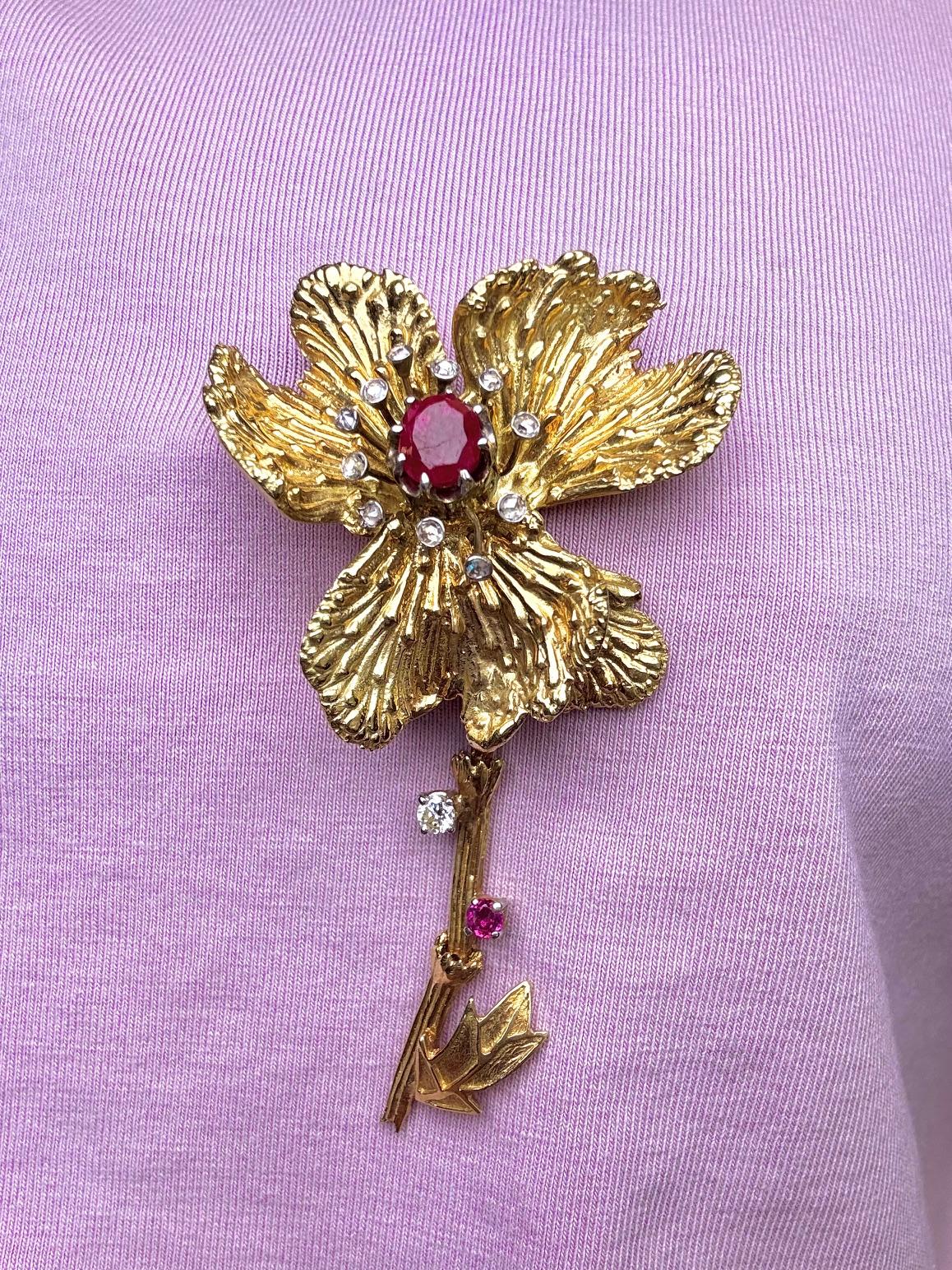 Cette broche florale sculpturale est réalisée en or jaune 14 carats et ornée d'un arrangement vibrant de rubis et de diamants. Au cœur de la fleur se trouve un rubis rouge foncé entouré d'autres rubis totalisant environ 1,87 carat. Des accents de