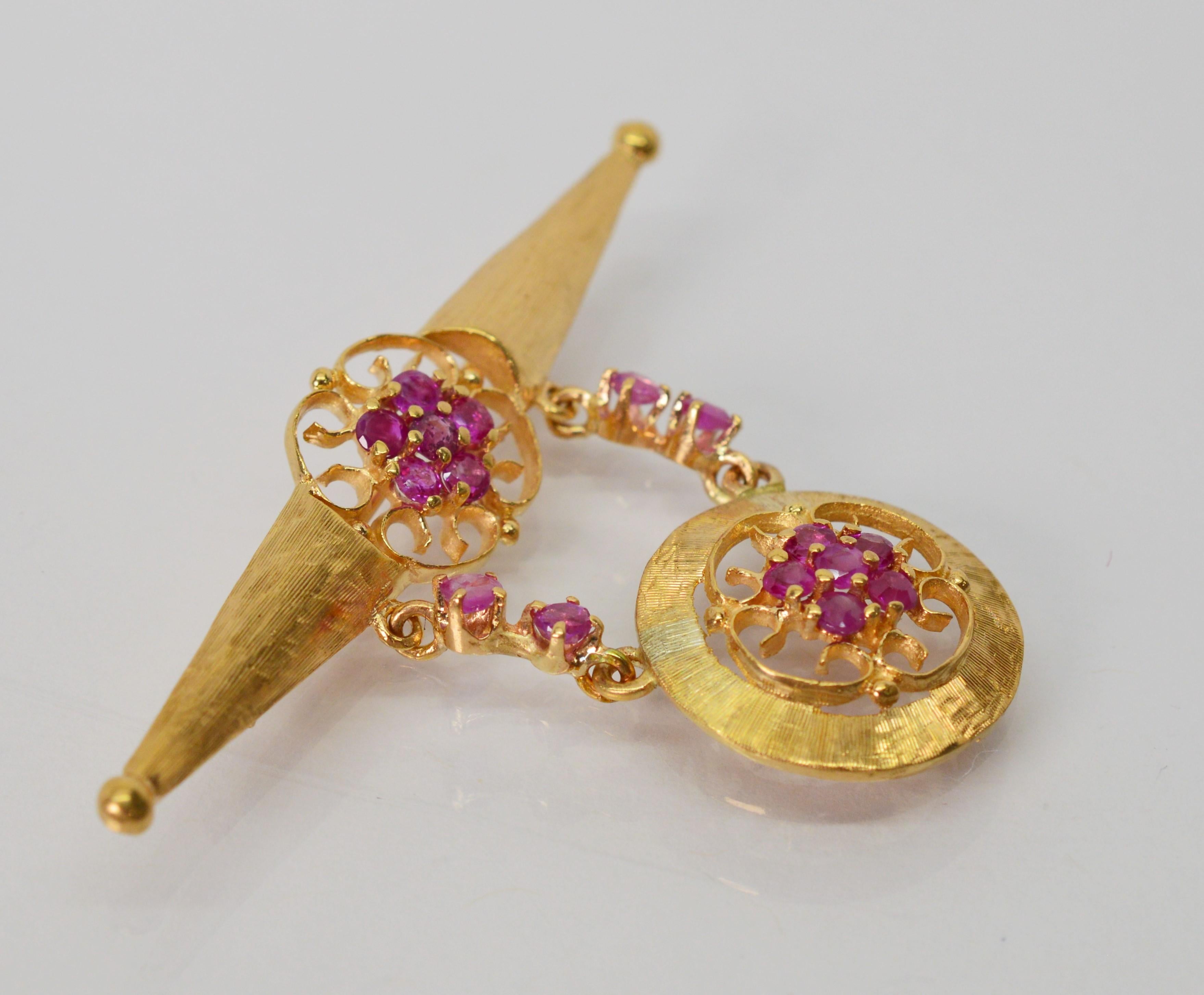 Floral ruby clusters framed in bright gold filigree soften the line of this romantic Art Deco fourteen karat 14K yellow gold bar pin brooch. The geometric bar pin hosts a suspended matching ruby floral charm in a round medallion shape  The top bar