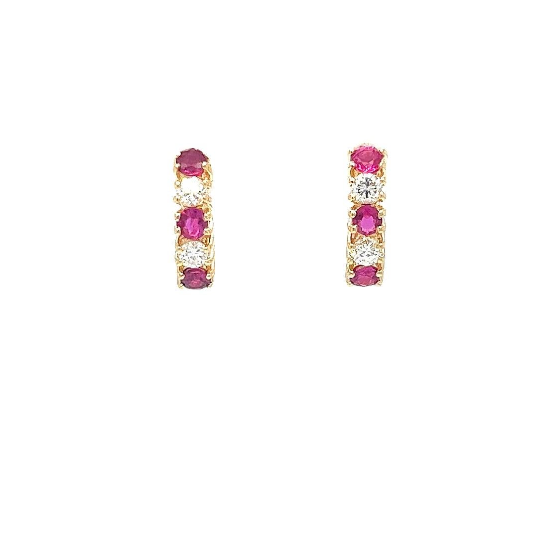 These elegant 14 karat yellow gold huggie hoop earrings feature a vibrant combination of richly colored rubies and sparkling diamonds. Each earring is set with 3 round rubies, totaling approximately 0.60 carats combined, known for their deep red hue