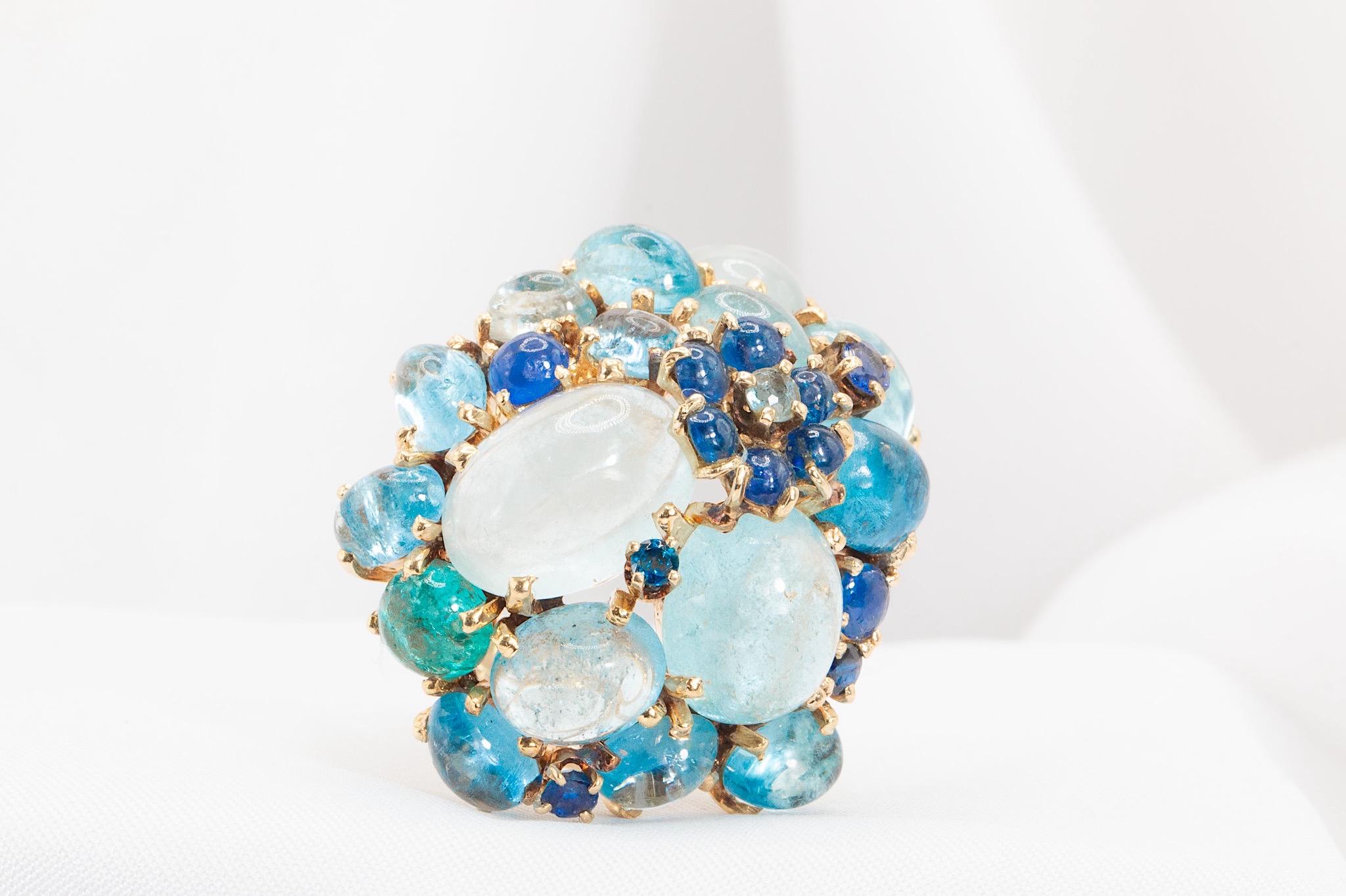 Cette bague unique en son genre est un véritable bijou ! Fabriqué en or 14k, il est orné d'un éventail de saphirs et d'aigues-marines taillés en cabochon, ce qui en fait une pièce audacieuse qui ne manquera pas de faire tourner les têtes.
