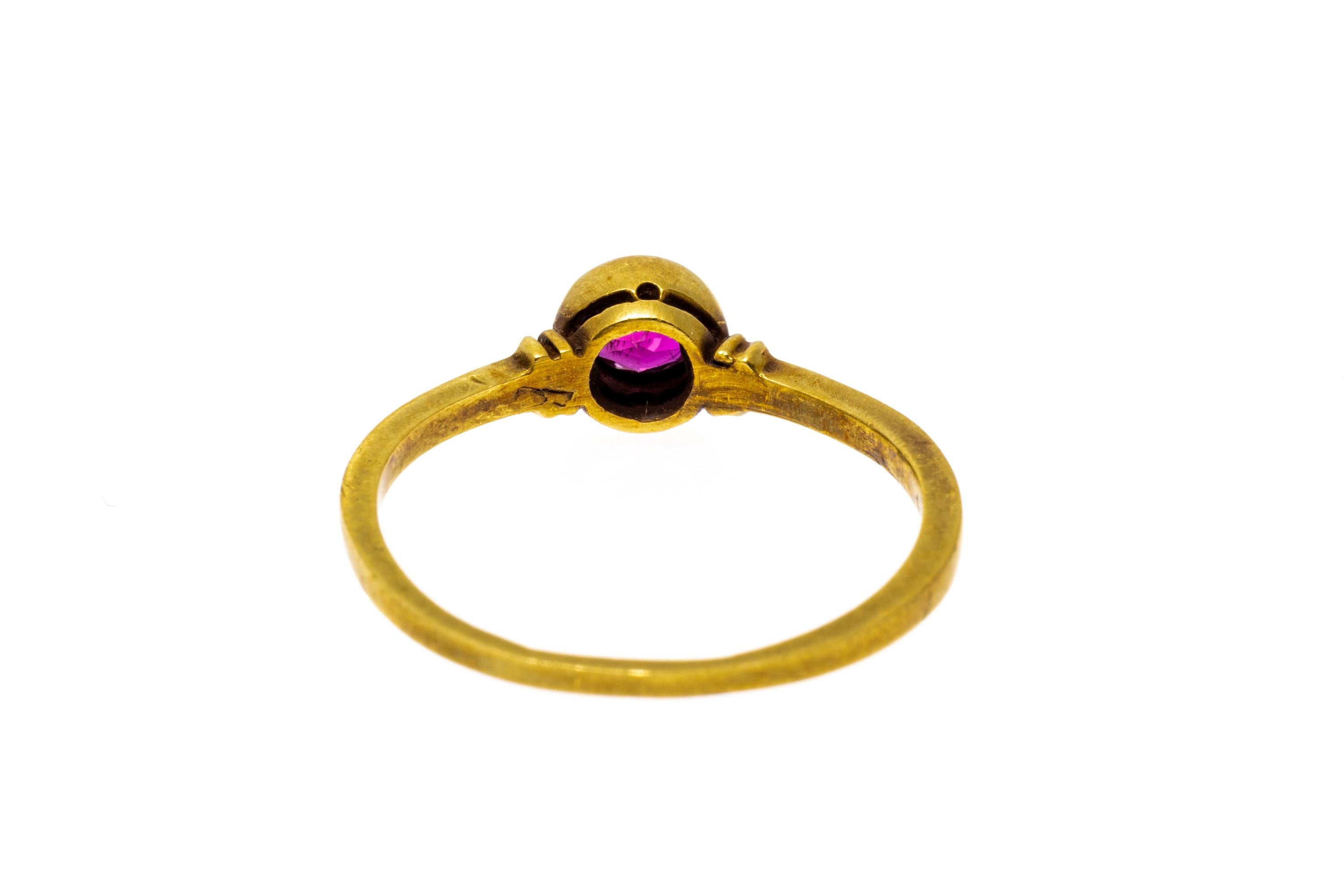 14k yellow gold ring. This pretty and simple ring is a burnished yellow gold, set in the center with a round faceted ruby, approximately 0.23 CTS, set into a high bezel and finished with ridged shoulders.
Marks: 14k
Dimensions: 9/32
