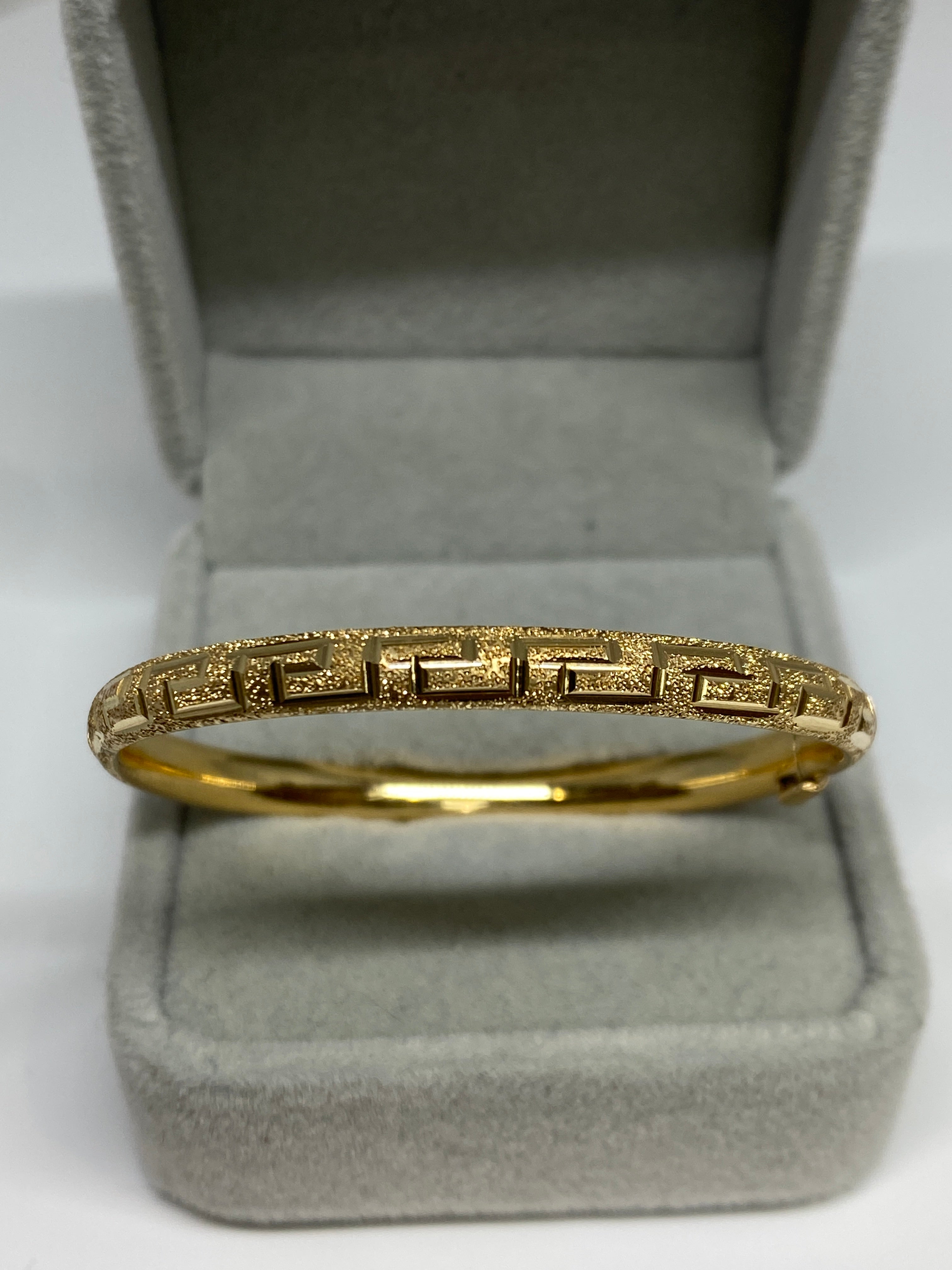 Charming small bangle in luminous 14k yellow gold.
It features a beautiful rounded convex shape with textured finish and classic etched greek key design.  Push clasp with under side safety catch

Stunning on it's own or worn in a stack.  This is a
