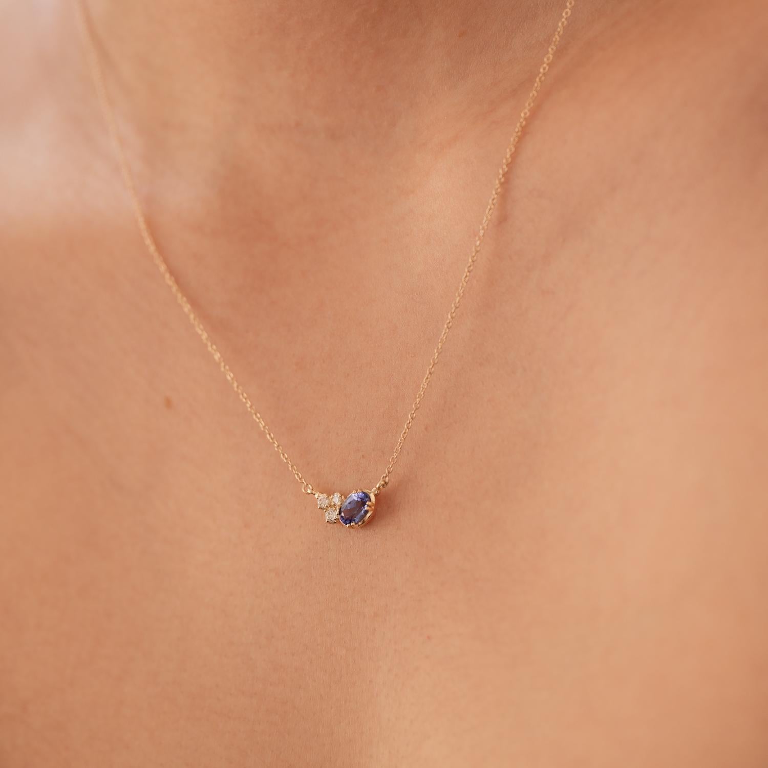 A delicate pendant with an asymetrical arrangement of stones including an oval tanzanite and three claw set diamonds like a celestial planet and its orbital moons. This handmade 14ct yellow gold pendant is hung on a fine 18