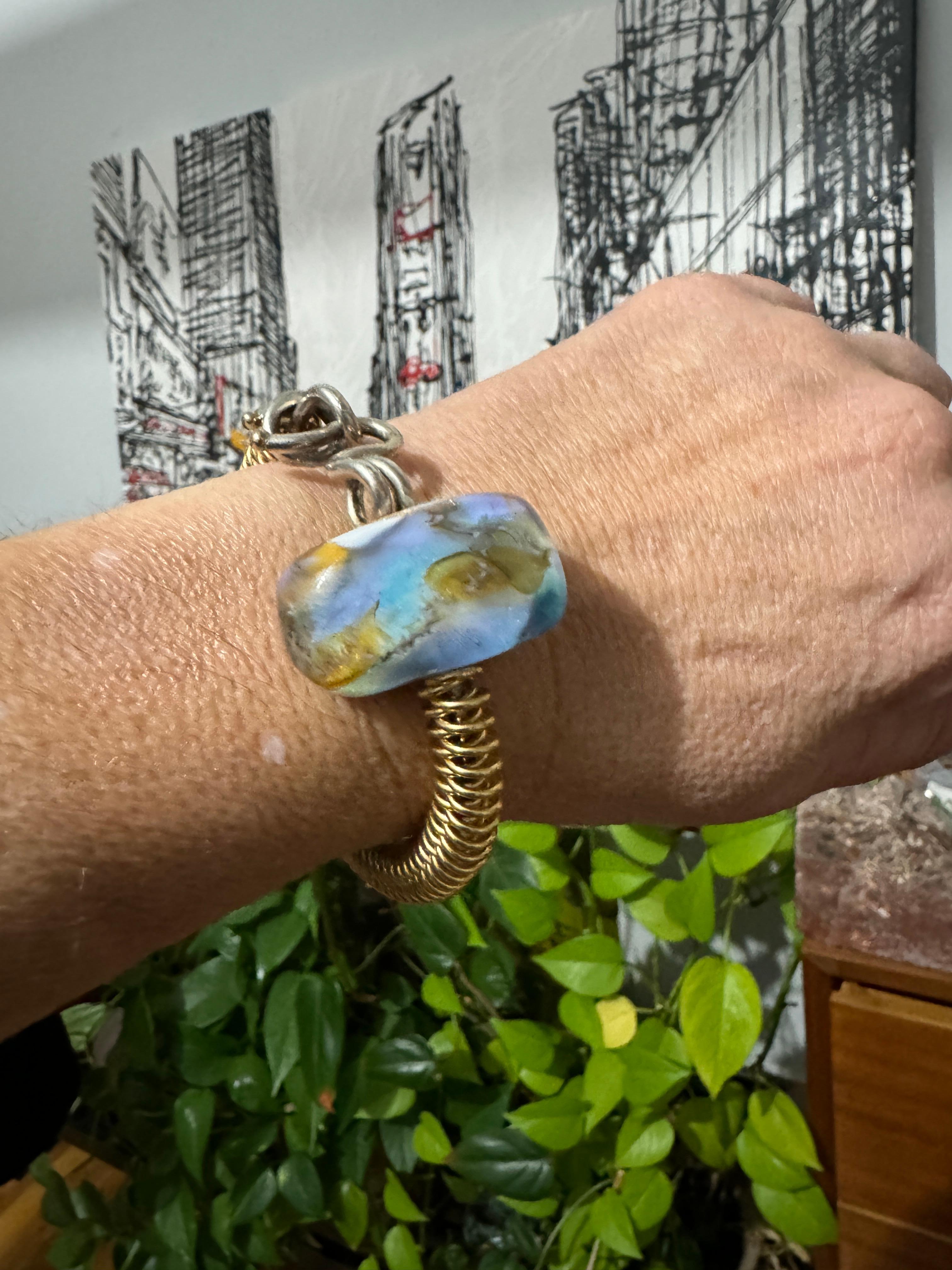 Kathleen Dennison 14k Gelbgold & Sterling Silber Armband. Gemischte Metalle bilden dieses handgefertigte, gewundene Armband mit einer großen Glasperle in der Mitte, die eine erstaunliche Farbgebung aufweist. Ich bin ein 6,5 Handgelenk und ich habe