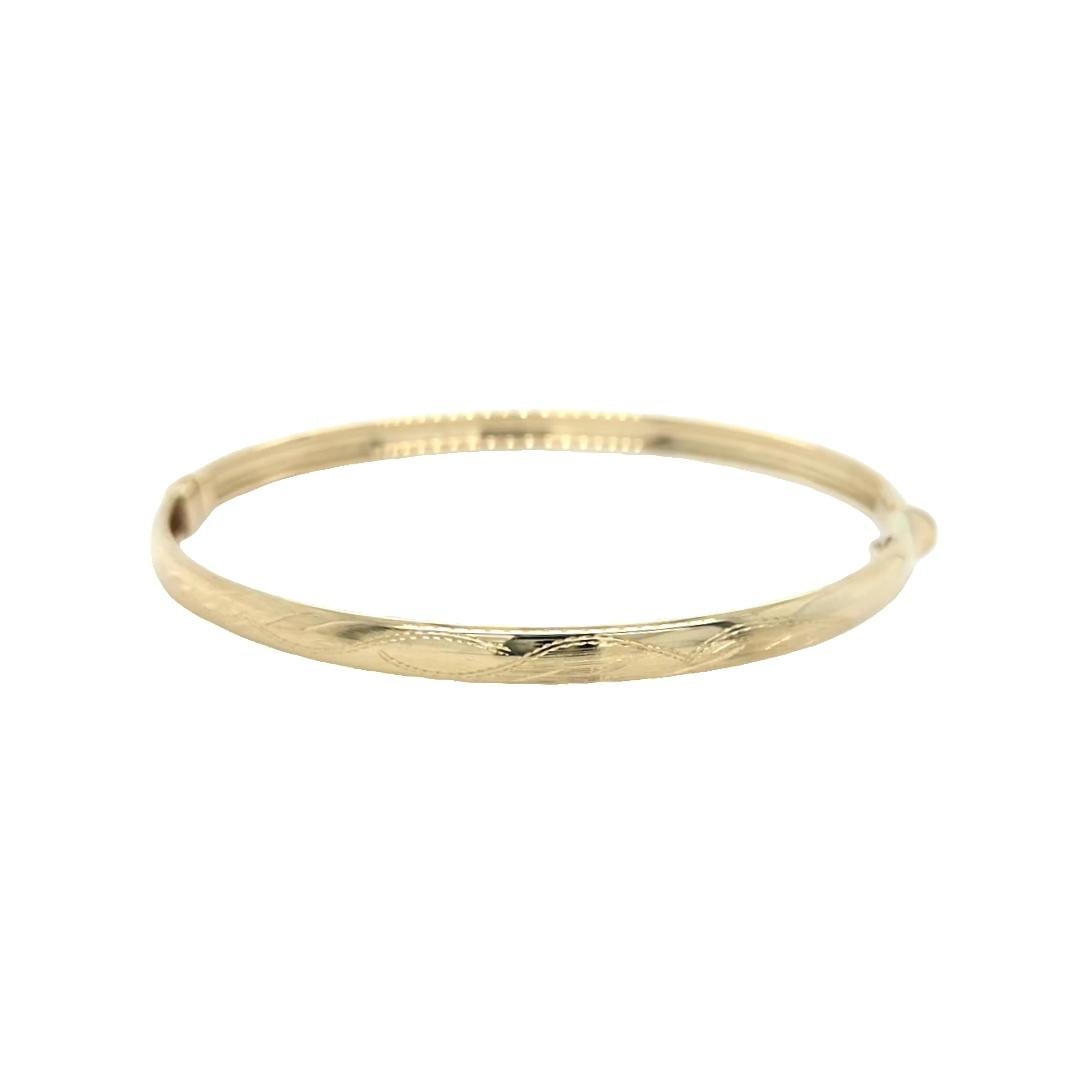 This classic 14 karat yellow gold textured bangle is a refined addition to any fine jewelry collection. Measuring 6.5 inches in length and 4.3mm in width, the bangle is detailed with a subtle texture that enhances the natural warmth of yellow gold,