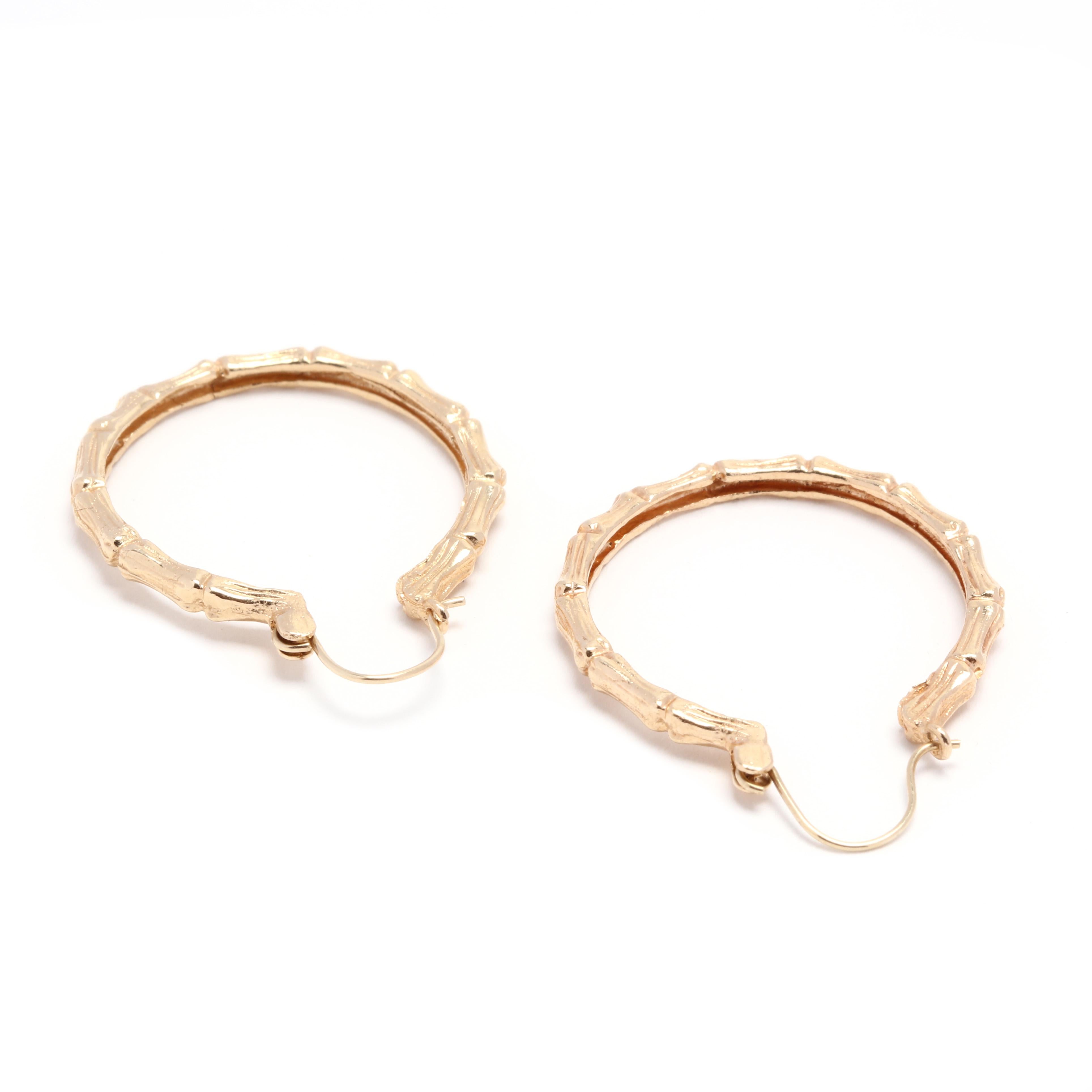 A pair of 14 karat yellow gold thin bamboo dangle hoop earrings. These earrings feature a thin bamboo motif design with a curved ear wire so that the hoops dangle slightly below the ear lobe.

Length: 1 in.

Width: 2.25 mm

2.95 dwts.

* Please note