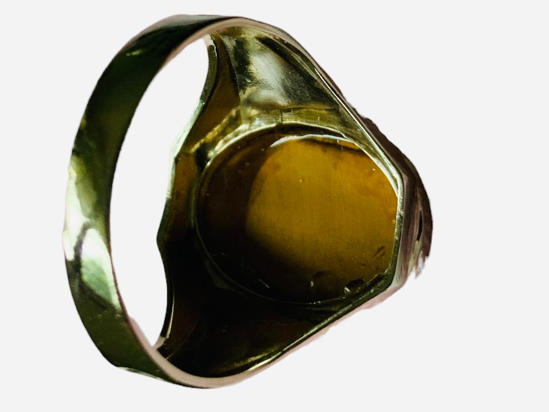 This is an 14K Yellow Gold Tiger’s Eye Cameo Ring. It depicts a white and yellow gold ring tiger’s eye oval cameo with the profile of a Roman soldier at the top of it. The center of the shanks is yellow gold and decorated with engraved leaves and
