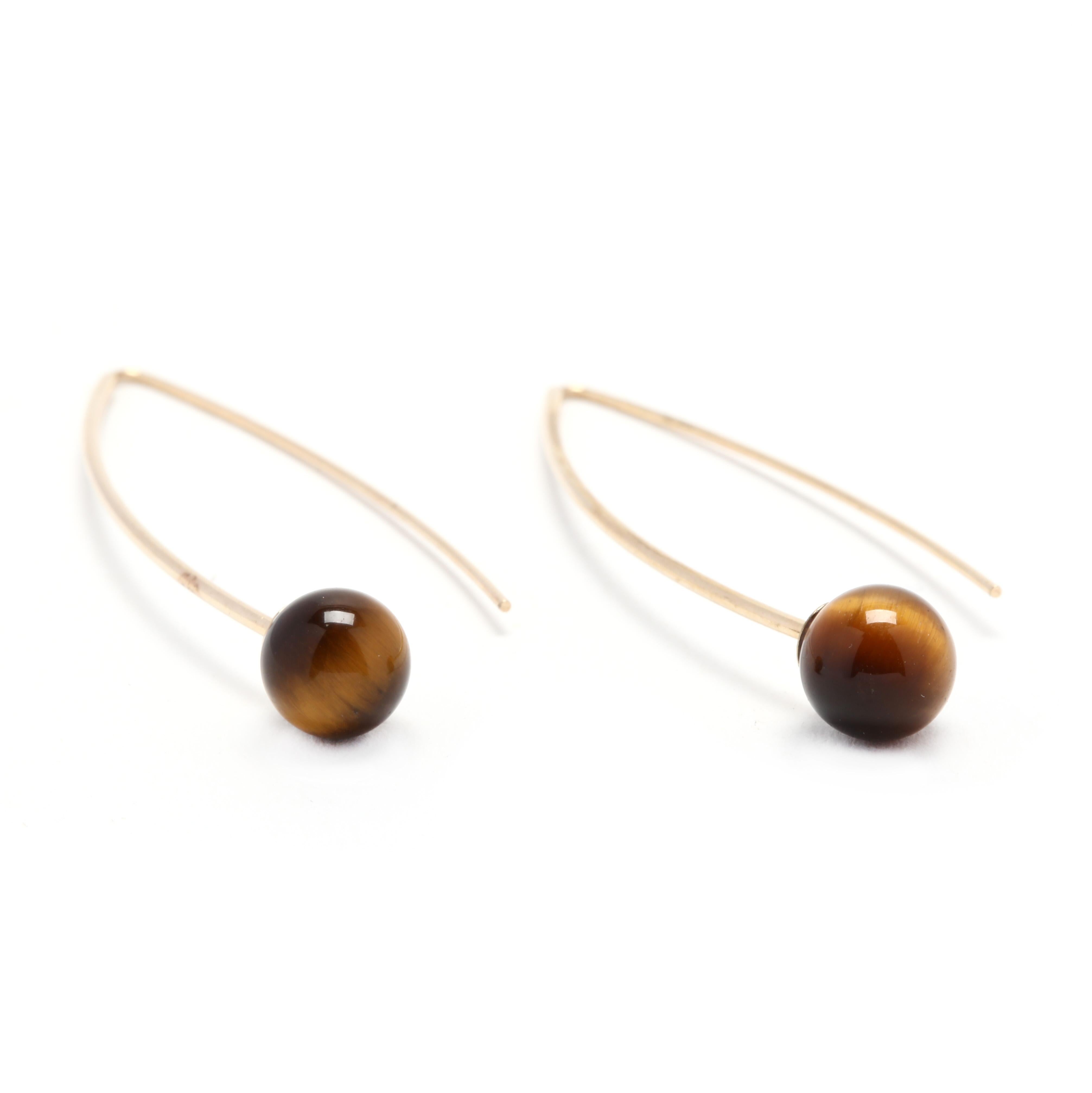 A pair of 14 karat yellow gold tiger's eye earrings. These earrings feature a navette ear wire shape with a round tiger's eye bead on each earring.

Stones:
- tiger's eye, 2 stones
- round bead
- 7.25 mm

Length: 1.75 in.

Width: 1/2 in.

1.2