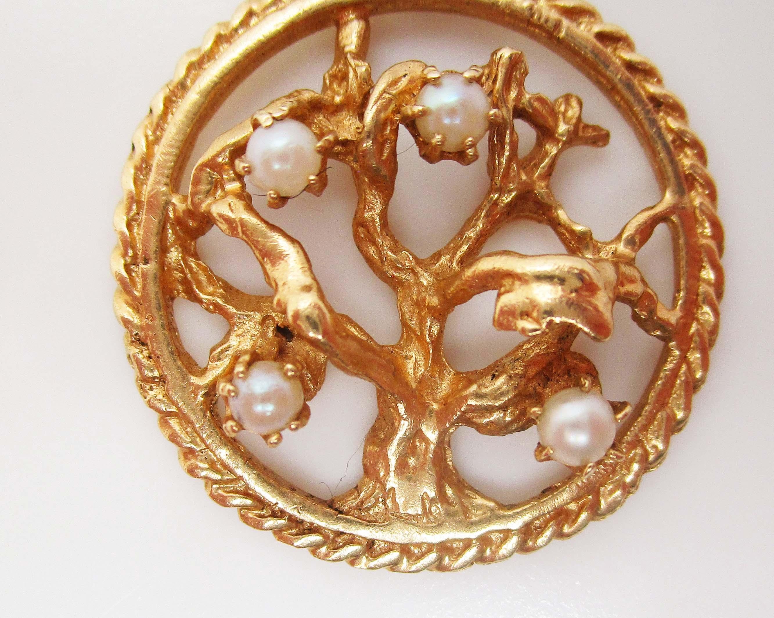 This is a gorgeous pendant in 14k yellow gold featuring an elegant tree of life motif decorated with bright white seed pearls. The pendant has a circular frame surrounding the tree design in the center, creating an element of negative space that