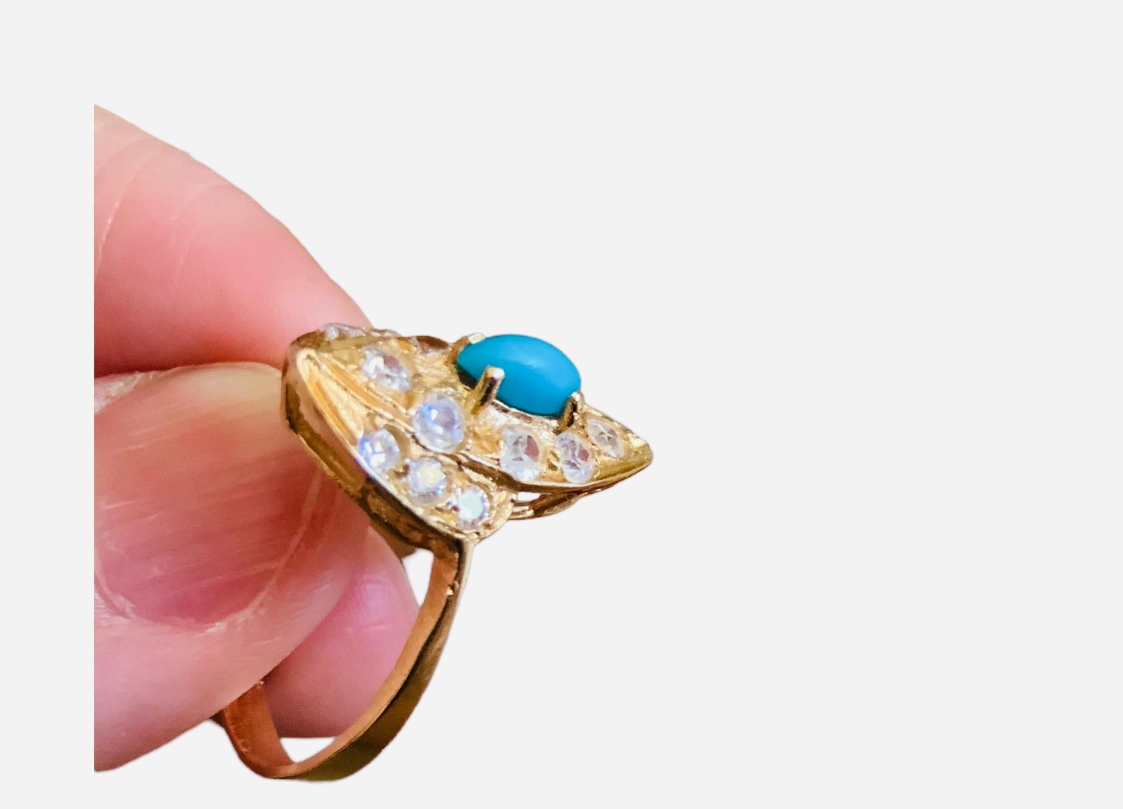 This is a 14K yellow gold turquoise sapphires ring. It depicts a navette shaped top decorated with a marquise shaped small turquoise in the center and surrounded by eight round small sapphires and six tiny round sapphires that are embedded. It is