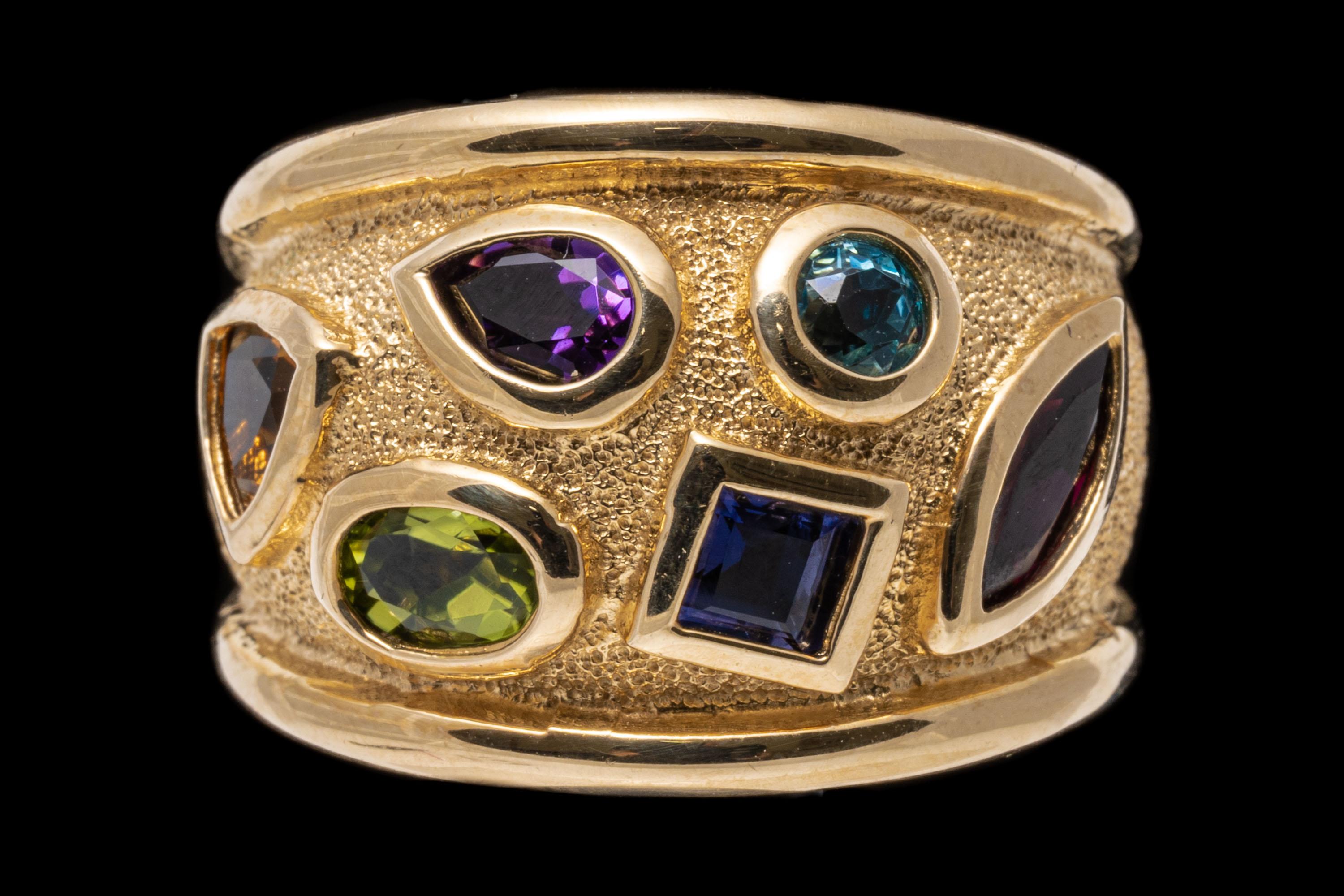 14k yellow gold ring. This beautiful, colorful, ultra-wide band ring features scattered, faceted gemstones displayed across the top, including an oval faceted, medium green peridot, approximately 0.28 CTS;  a trillion faceted, dark to medium yellow