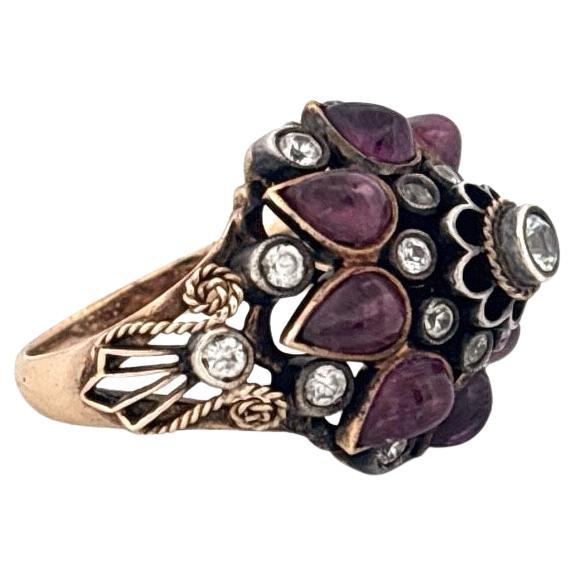 Este llamativo anillo vintage es una mezcla magistral de arte y elegancia, elaborado en oro amarillo de 14 quilates con un remate de plata. Presenta un diseño ornamentado y multidimensional, con lustrosos granates talla pera dispuestos en un
