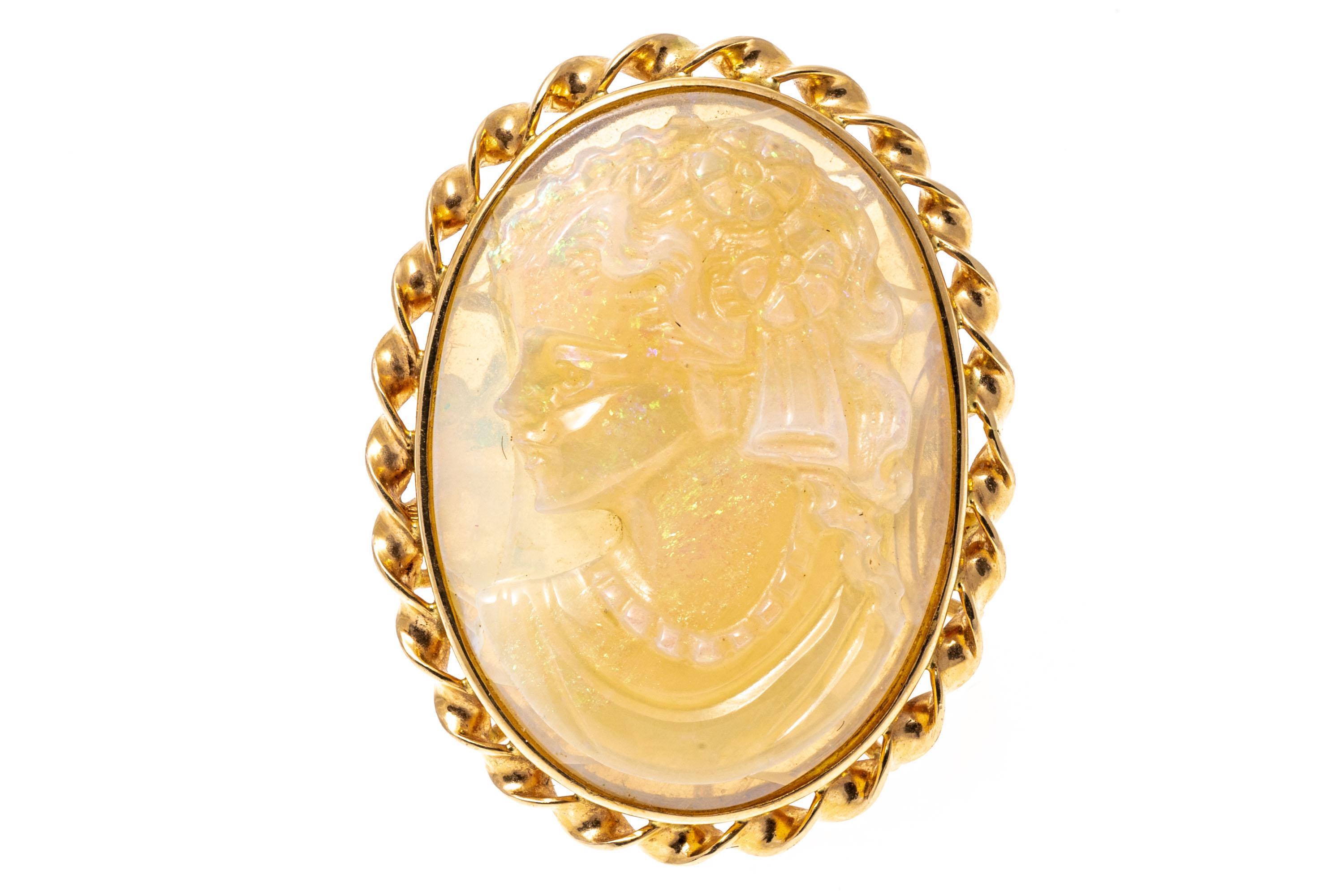 14k yellow gold ring. This beautiful, unusual vintage oval cameo ring is a white opal, with green plays of color, which features a lovely draped profile bust, facing to the left with decorated hair. The cameo is set off with a twisted gold frame,