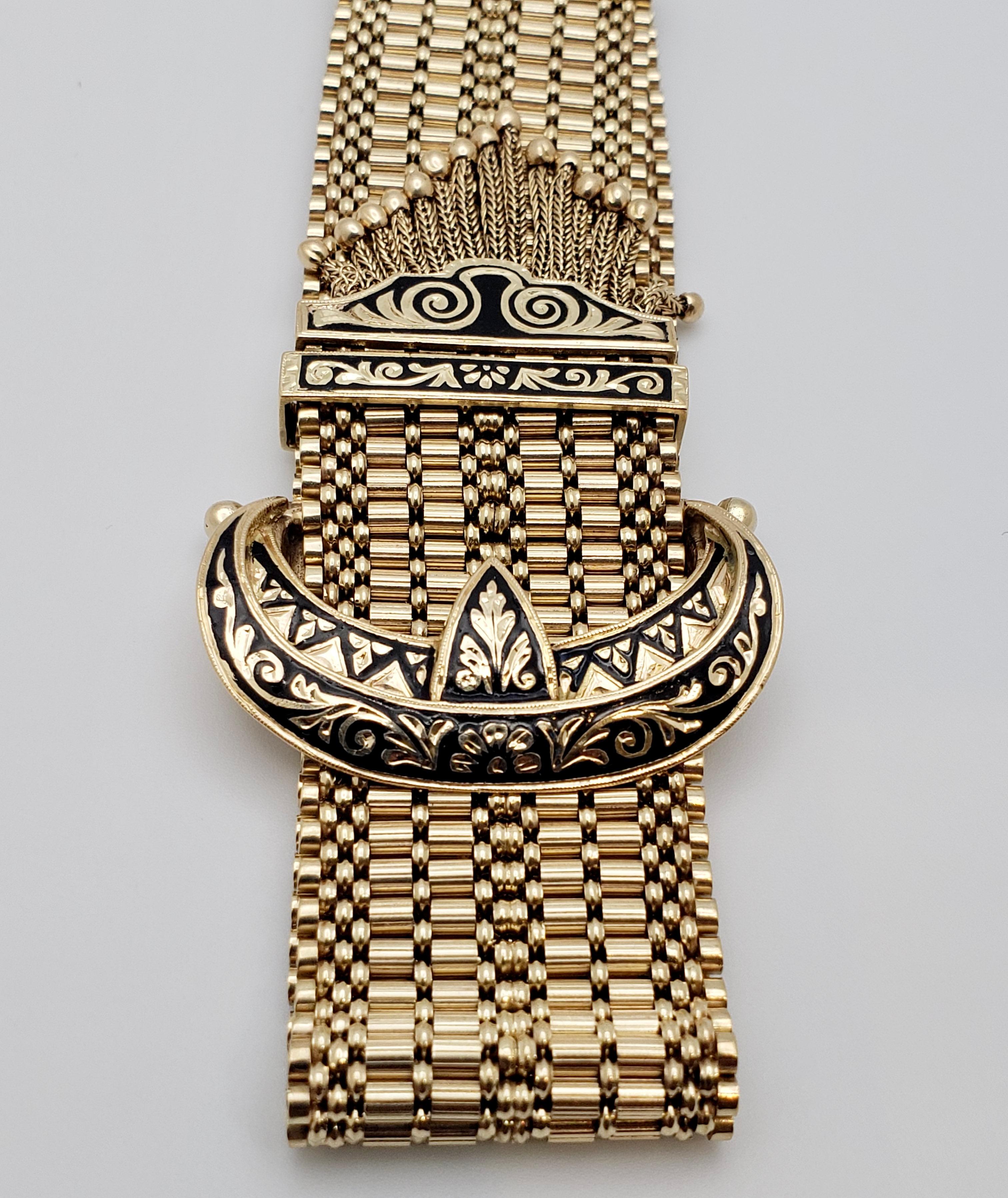 An authentic 14K yellow gold Victorian enamel tassle bracelet. The gold-mesh bracelet ends off with multi-fringed tassel and is mounted with a crescent moon-shaped slide-clasp, decorated with black enamel, which is used to adjust the length of the