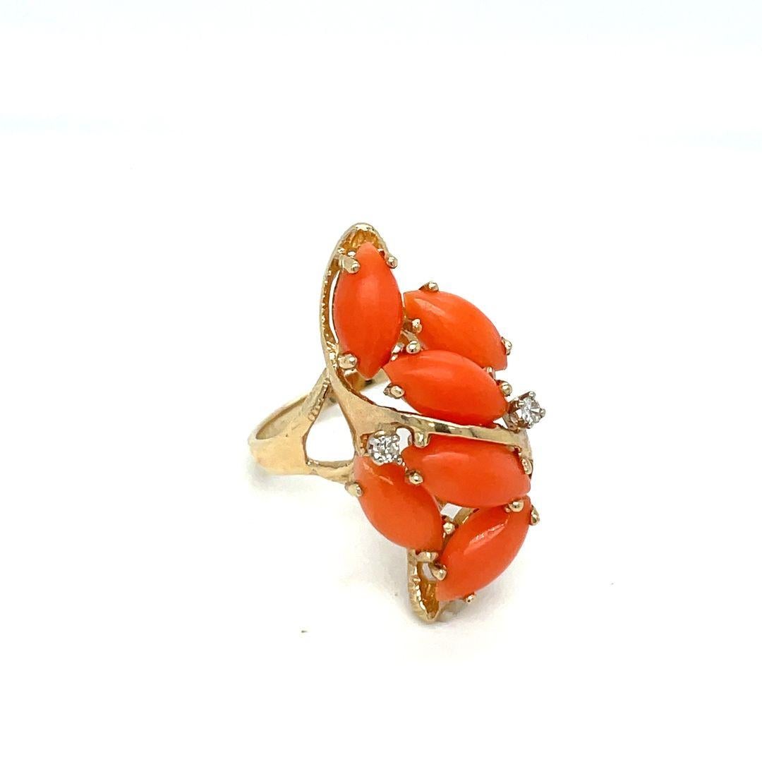 Cette belle bague vintage en or jaune 14k, présente six pierres de corail cabochon marquise orange rougeâtre, chacune mesurant environ 10 mm x 5 mm. En outre, la bague brille par la beauté de deux diamants ronds de taille brillant, d'une taille