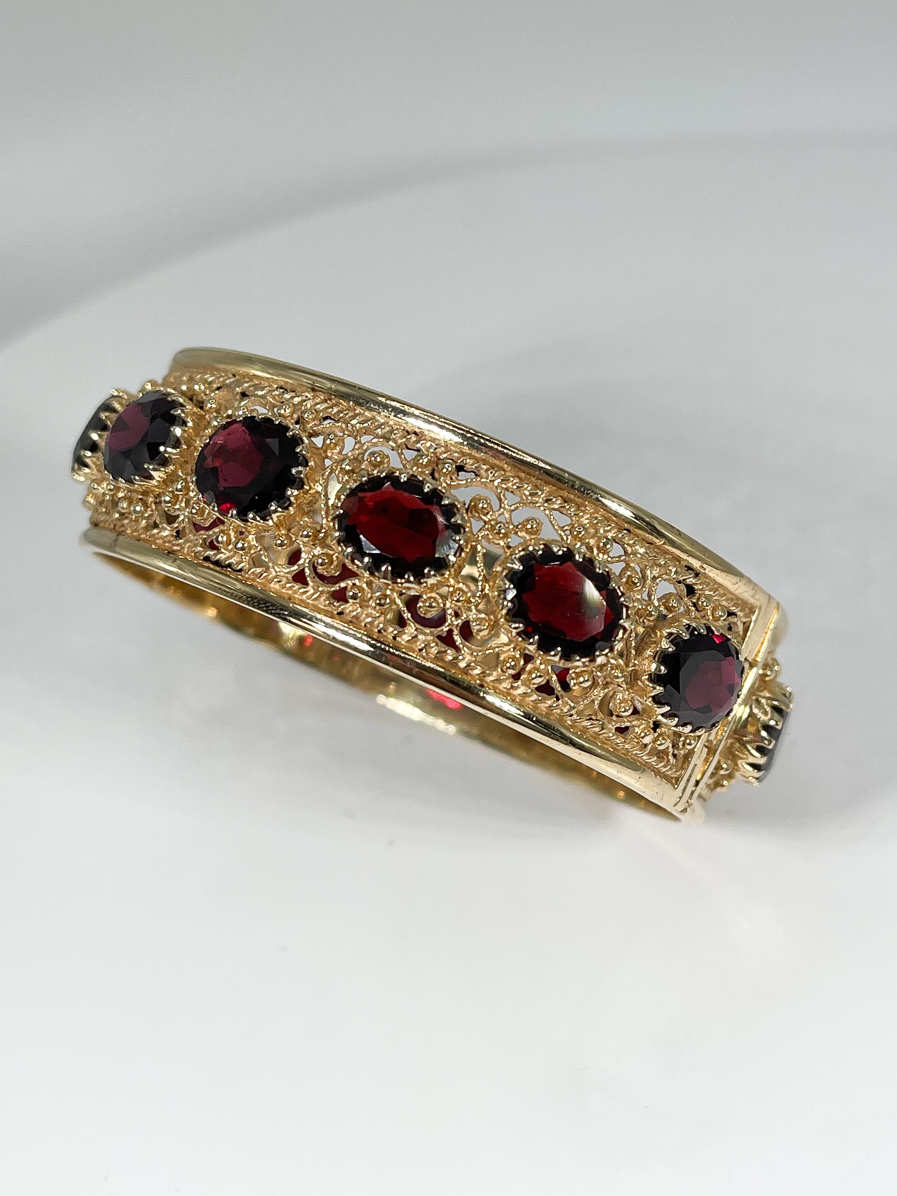 Fancy 14k yellow gold wide bangle with 14 8x10 oval Mozambique garnets. The bangle has a figure 8 clasp and push button to open for wearing. Has an inside diameter of about 7 3/4'' and a weight of 55.6 grams.