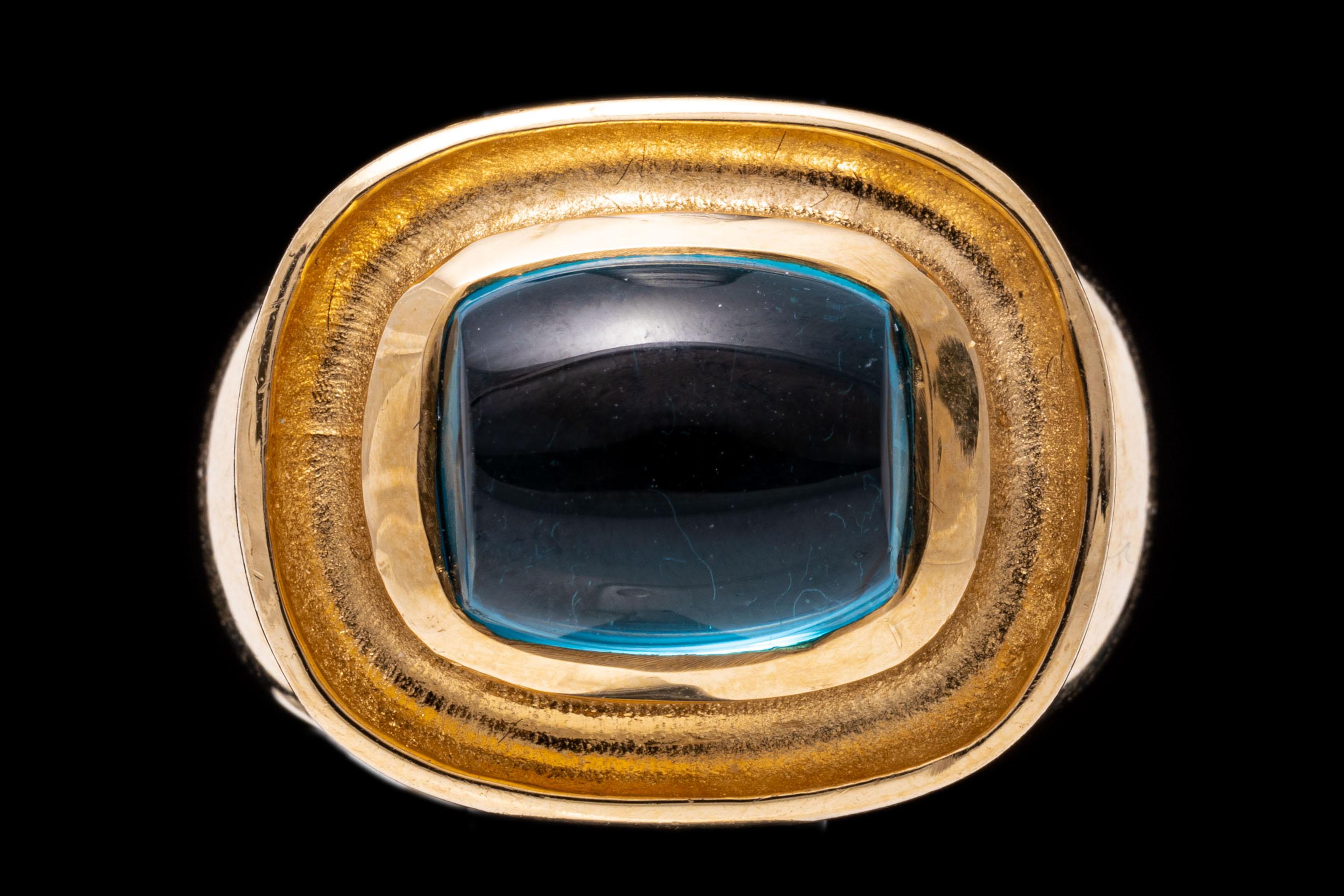14k yellow gold ring. This beautiful ring has a horizontal, rectangular sugarloaf cabachon cut medium to light blue color blue topaz center, bezel set int a grooved, rounded rectangular contemporary profile, finished with wide, high polished