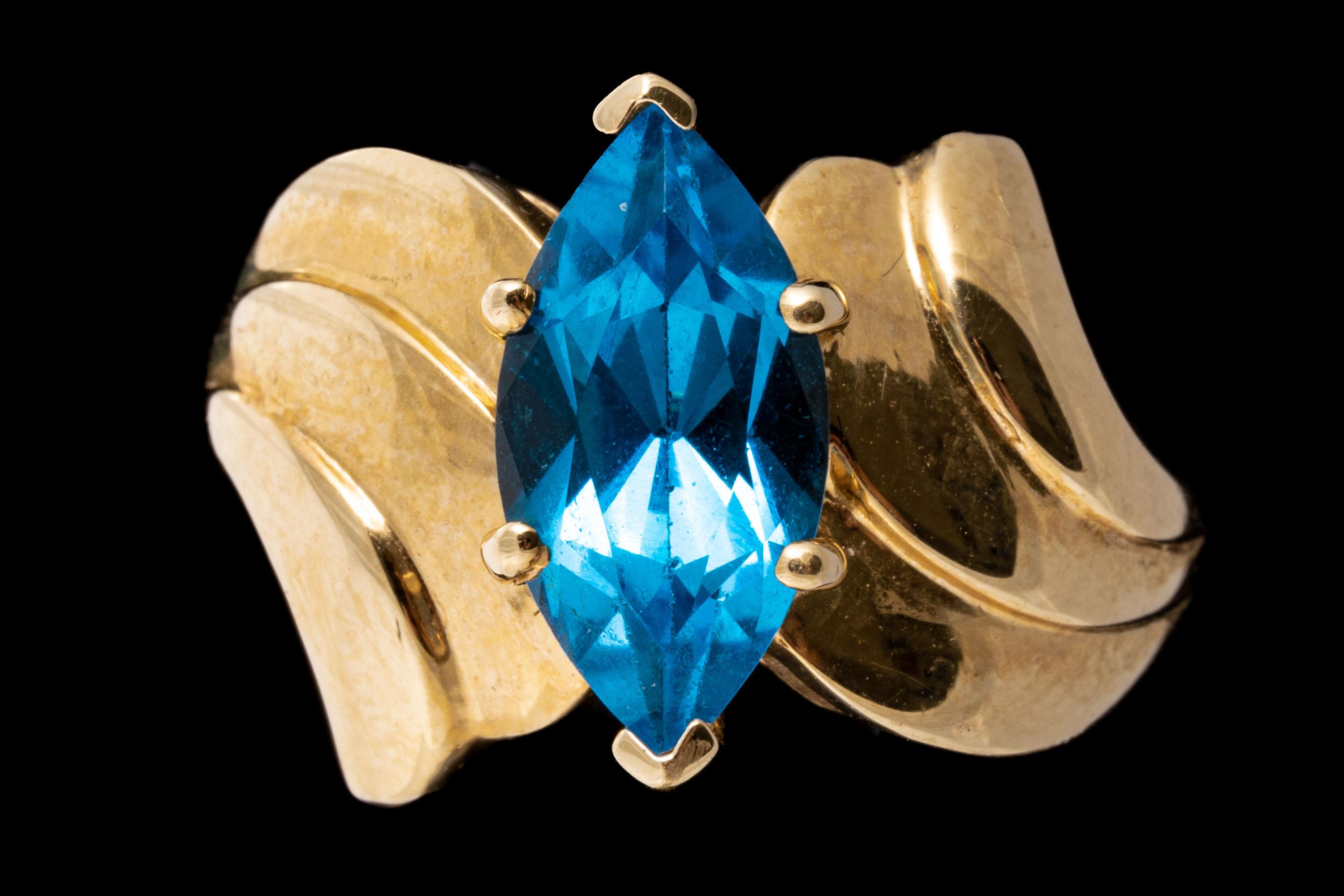 14k yellow gold ring. This striking ring has wide, ribbed bypass style shoulders, set in the center with a marquise faceted, London blue color blue topaz, prong set, approximately 1.87 CTS.
Marks: 14k
Dimensions: 1/4