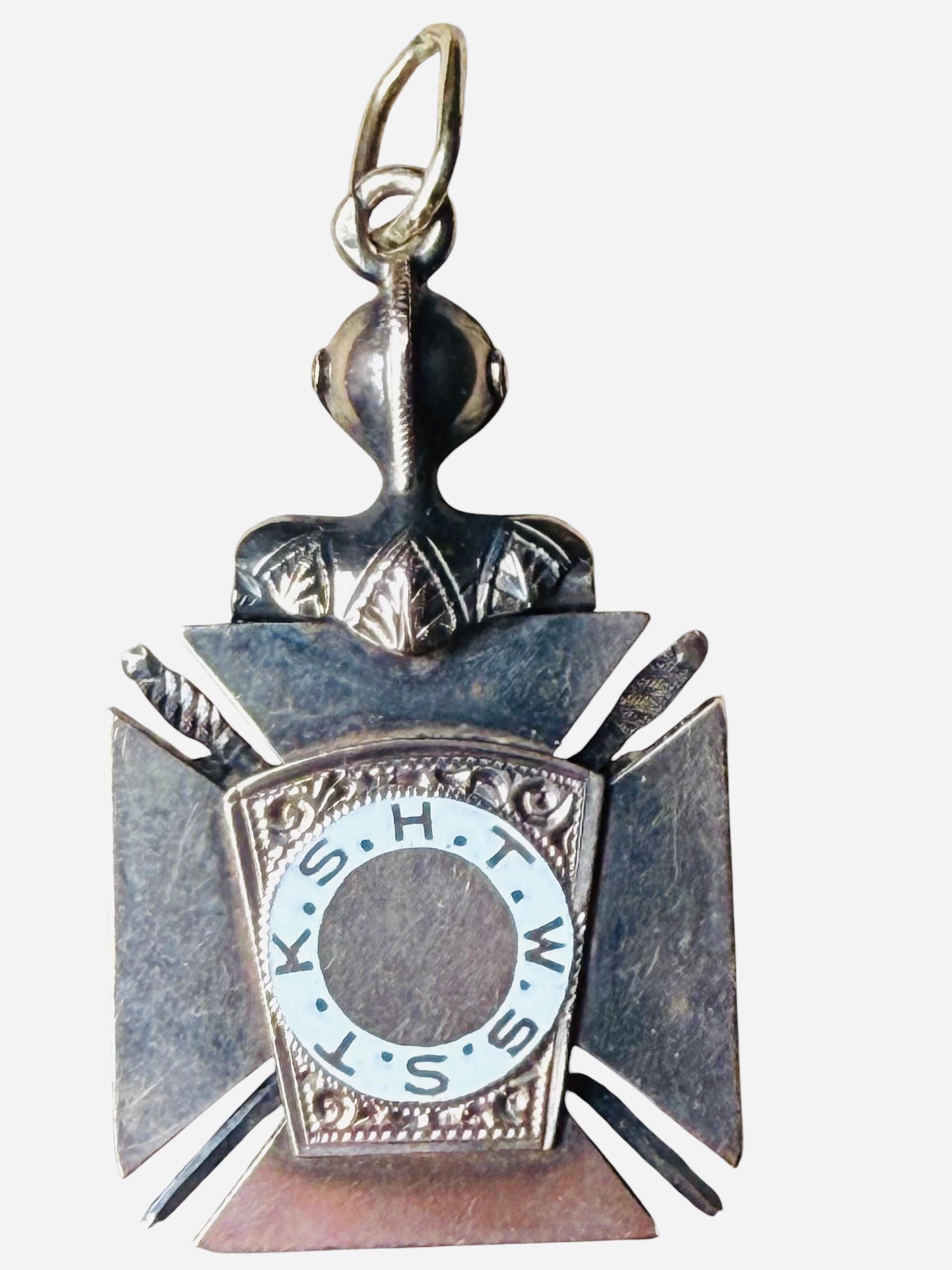 This is a 14K yellow/white gold and enamel Masonic pendant. The pendant is shaped as a Maltese Cross. Above the black color enamel cross, there is a knight helmet and part of a breastplate. In the center, there is a red color enamel cross and in