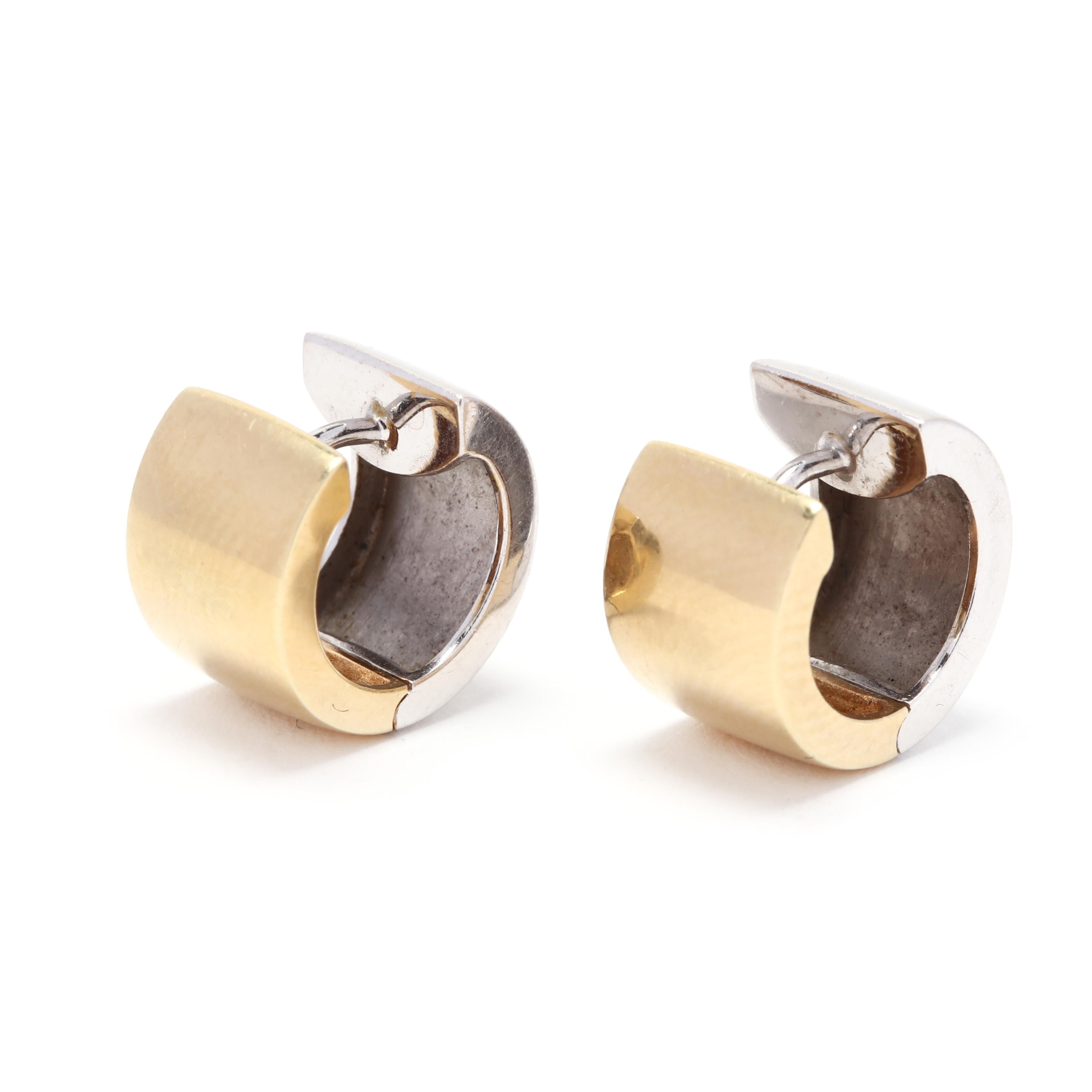 A pair of 14 karat yellow and white gold huggie hoop earrings. These earrings feature a flat wide, huggie hoop design with white gold on one side and yellow gold on the other. These earrings are about the size of a dime and can be worn to show