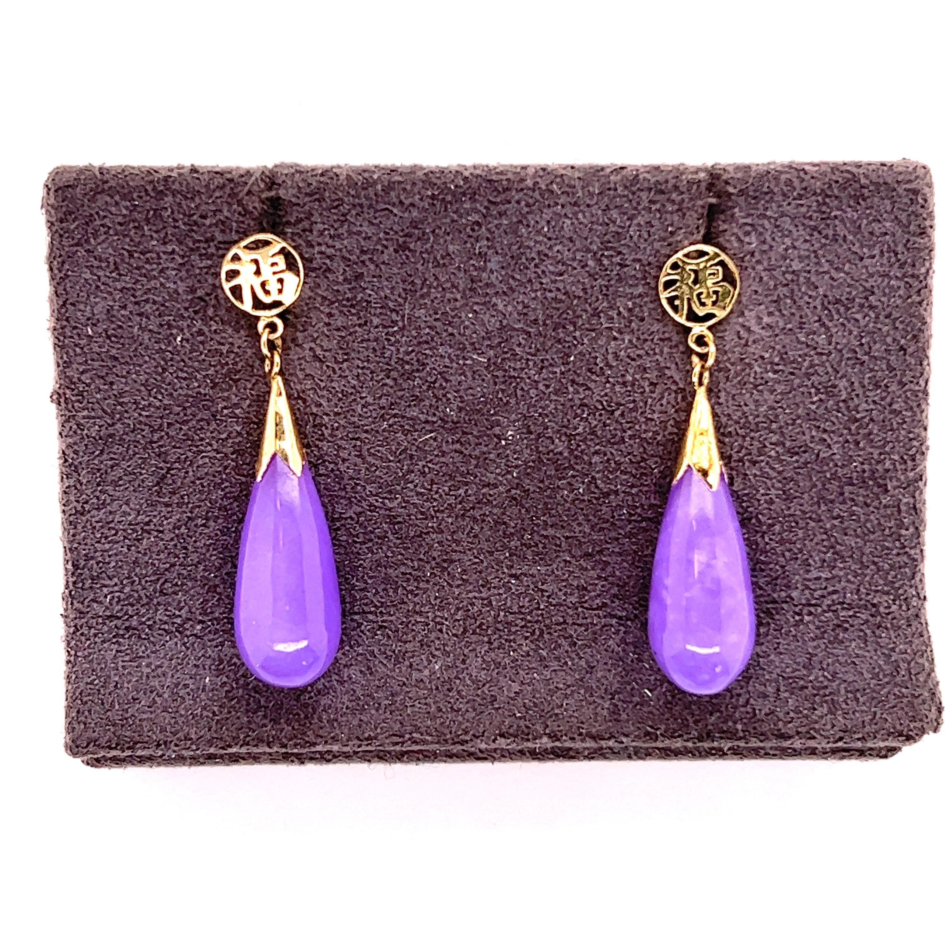 14kt yellow gold pendulum earrings. The earrings contain one round yellow gold portion at the top of the earrings made into a kanji (good luck symbol). Suspended from the top kanji are smooth and sleek pendulums of purple jade. The purple jade has