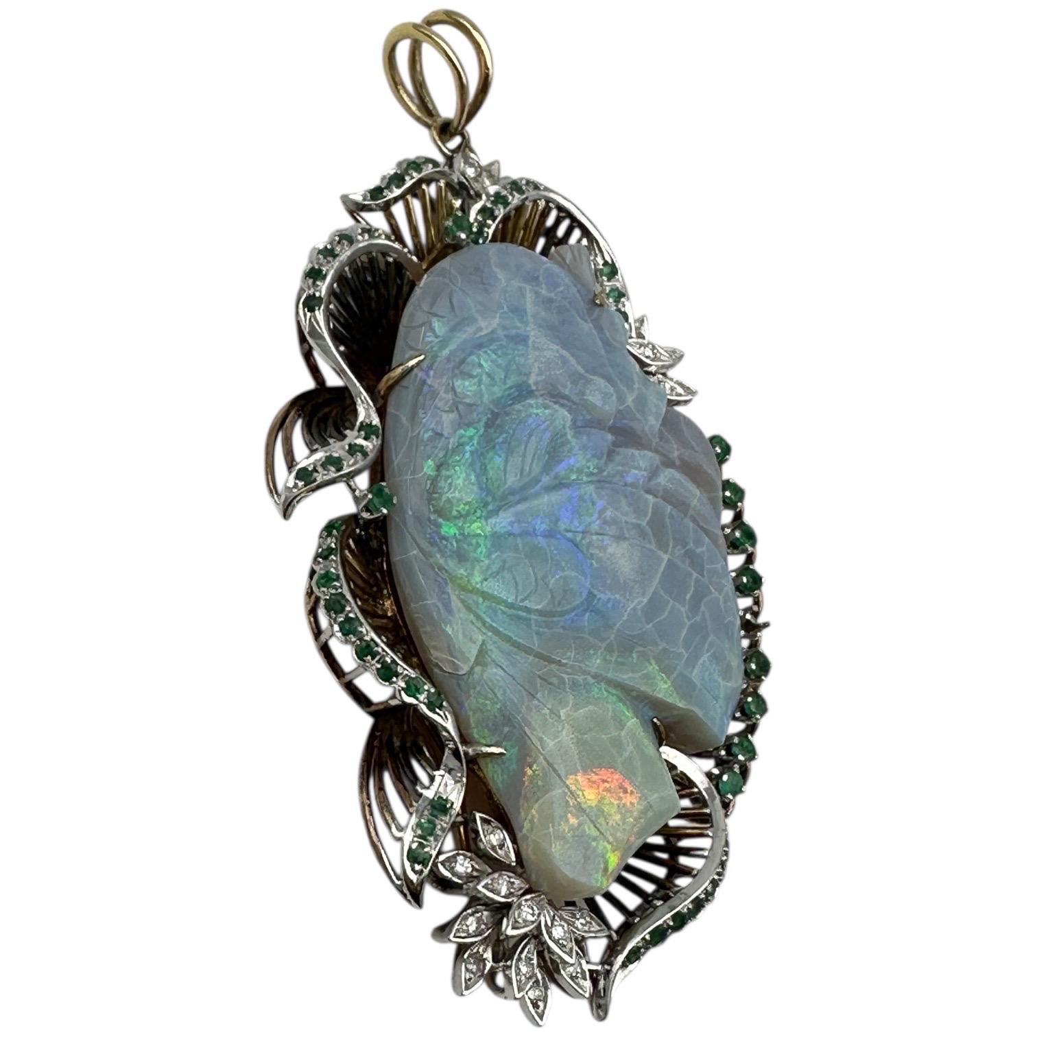 L'immagine mostra un intricato ciondolo a forma di pesce carpa.
Il ciondolo presenta al centro una grande gemma opale intagliata, raffigurante una carpa o un pesce koi. La pietra è incastonata in una cornice di metallo, probabilmente oro bianco o