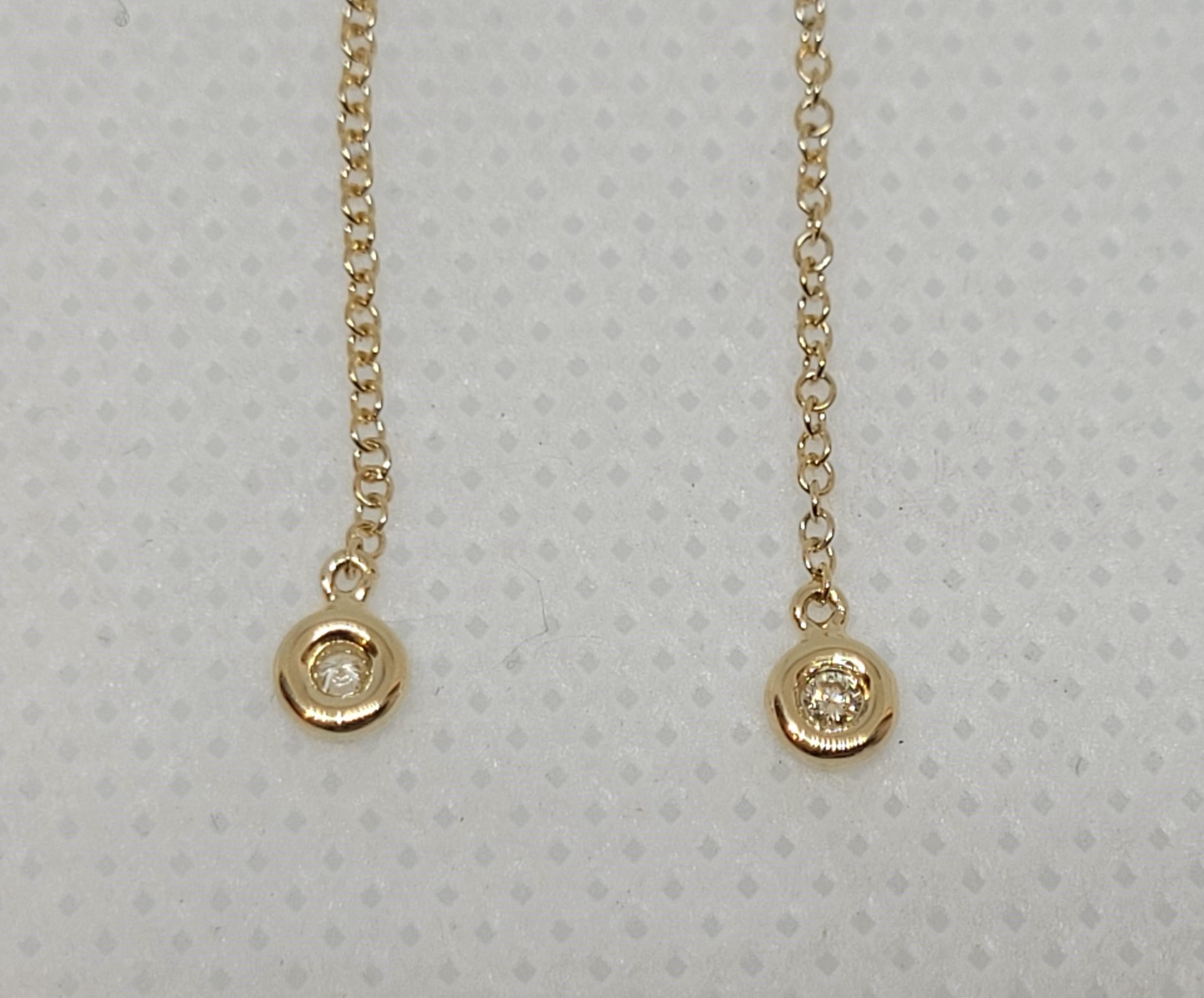14kt yellow gold thread-style chain earrings with two bezel set round brilliant diamonds of approximately .04cttw. The diamonds are G/H color and SI clarity. The chain is a round link, stamped 14kt yellow gold, stamped with a designer symbol, and