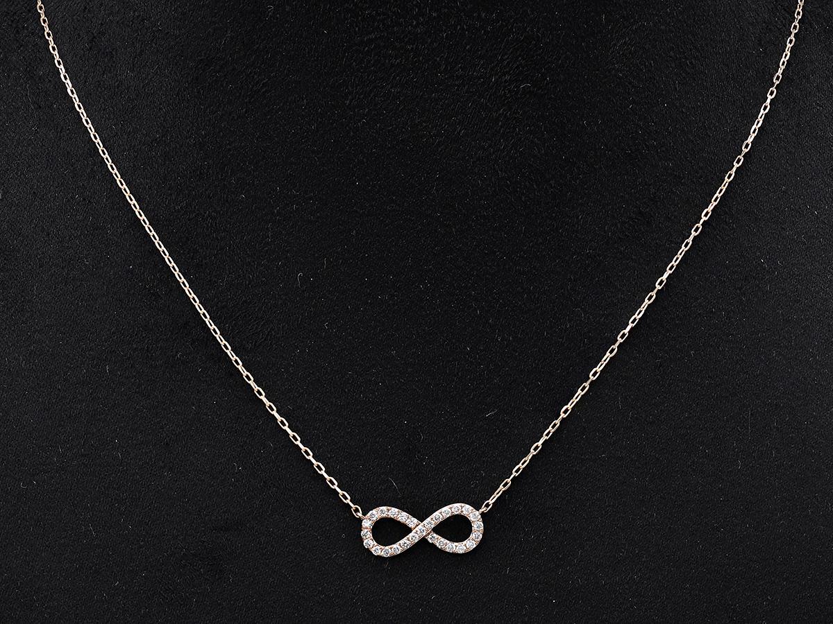 Le pendentif présente l'élégant symbole du huit couché à l'horizontale, ou lemniscate, qui représente quelque chose qui n'a ni début ni fin. La surface du symbole est recouverte de petits diamants ronds sertis en pavé qui maximisent l'éclat et la