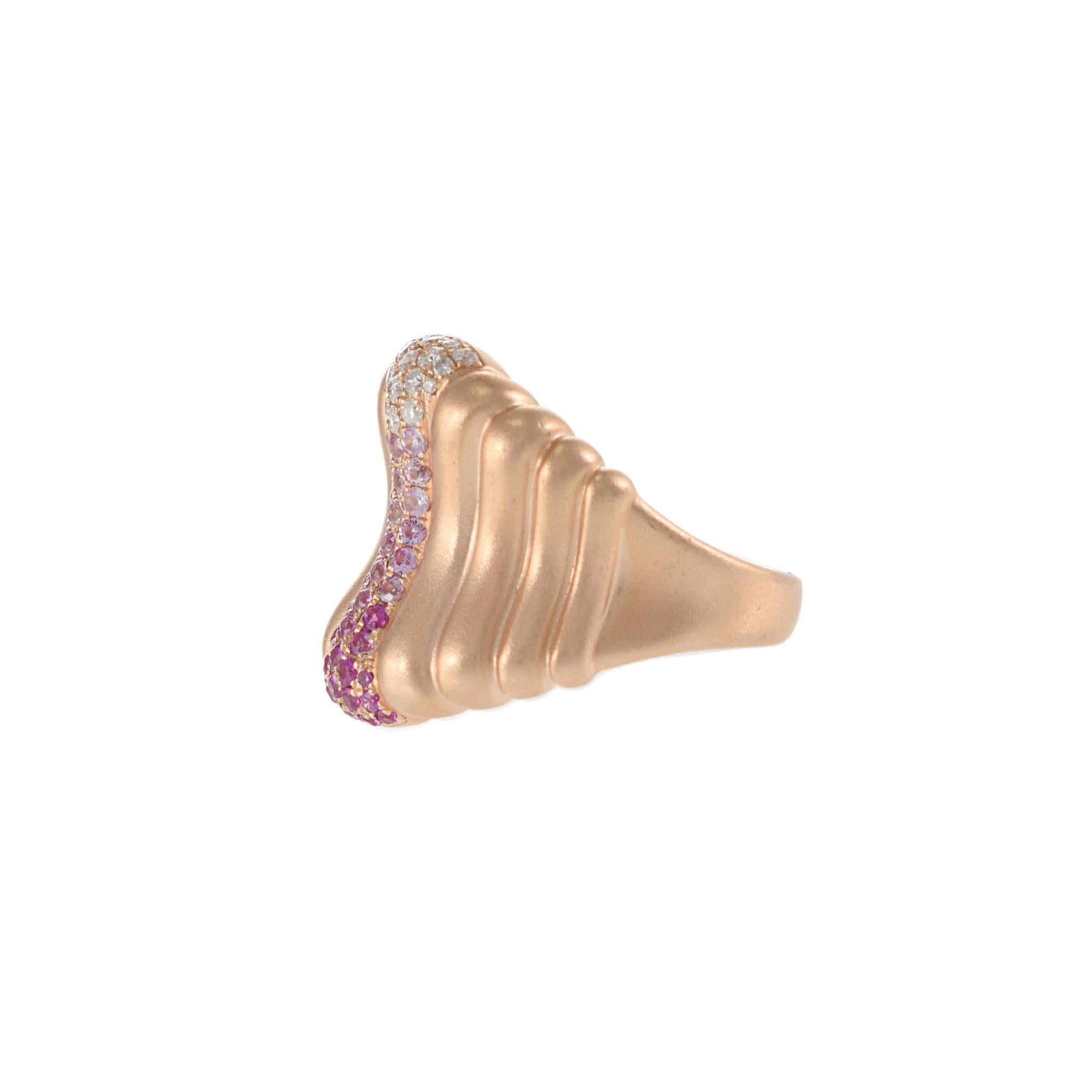 Une version sculpturale d'un classique audacieux. Cette bague cigare en or rose 14KT présente un design ondulé et profilé accentué par une vague verticale de saphirs roses qui passent du violet profond au blush, ponctuée de diamants ronds de taille