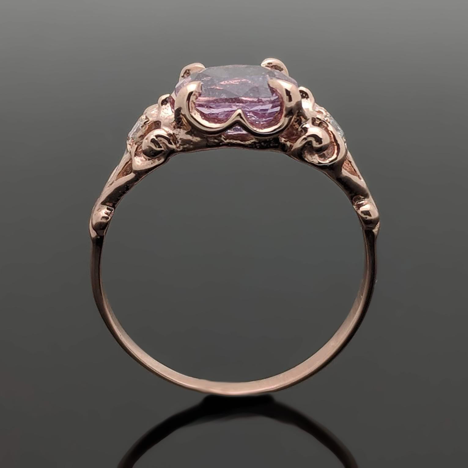 This 14kt rose gold ring is set with a large oval, pink sapphire with an estimated weight of 1.67ct. with 4 claw prongs. The detail includes a diamond on each side with an estimated 0.02 cttw. Estimated weight of gold is 1 gr. 

We will size it for