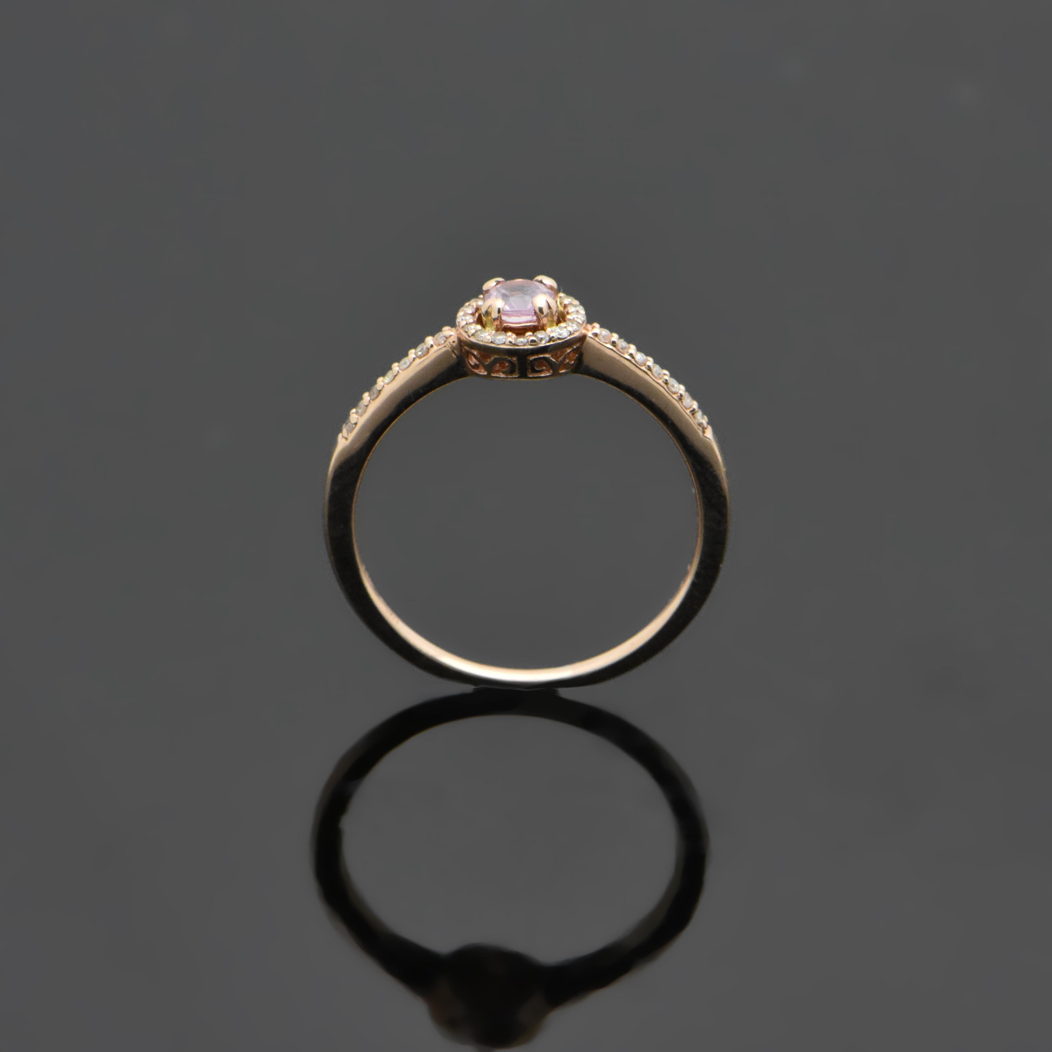 This petite 14kt rose gold ring features a pink sapphire with an estimated weight of 0.16ct. The sapphire is surrounded by a halo of diamonds as well as diamonds down each shank. The diamonds are estimated at 0.11cttw. Estimated weight of gold is
