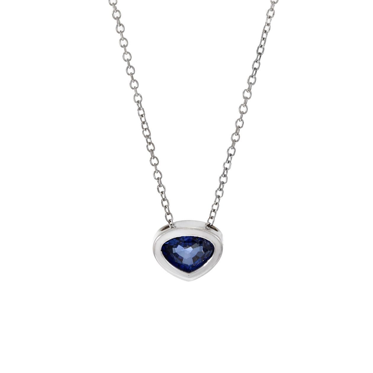 This 14KT white gold pendant necklace is a stylish and minimalist piece of jewelry, featuring a genuine blue sapphire with a unique triangular cut. The sapphire weighs 0.35 carats and is securely set in a bezel setting, adding to the modern and