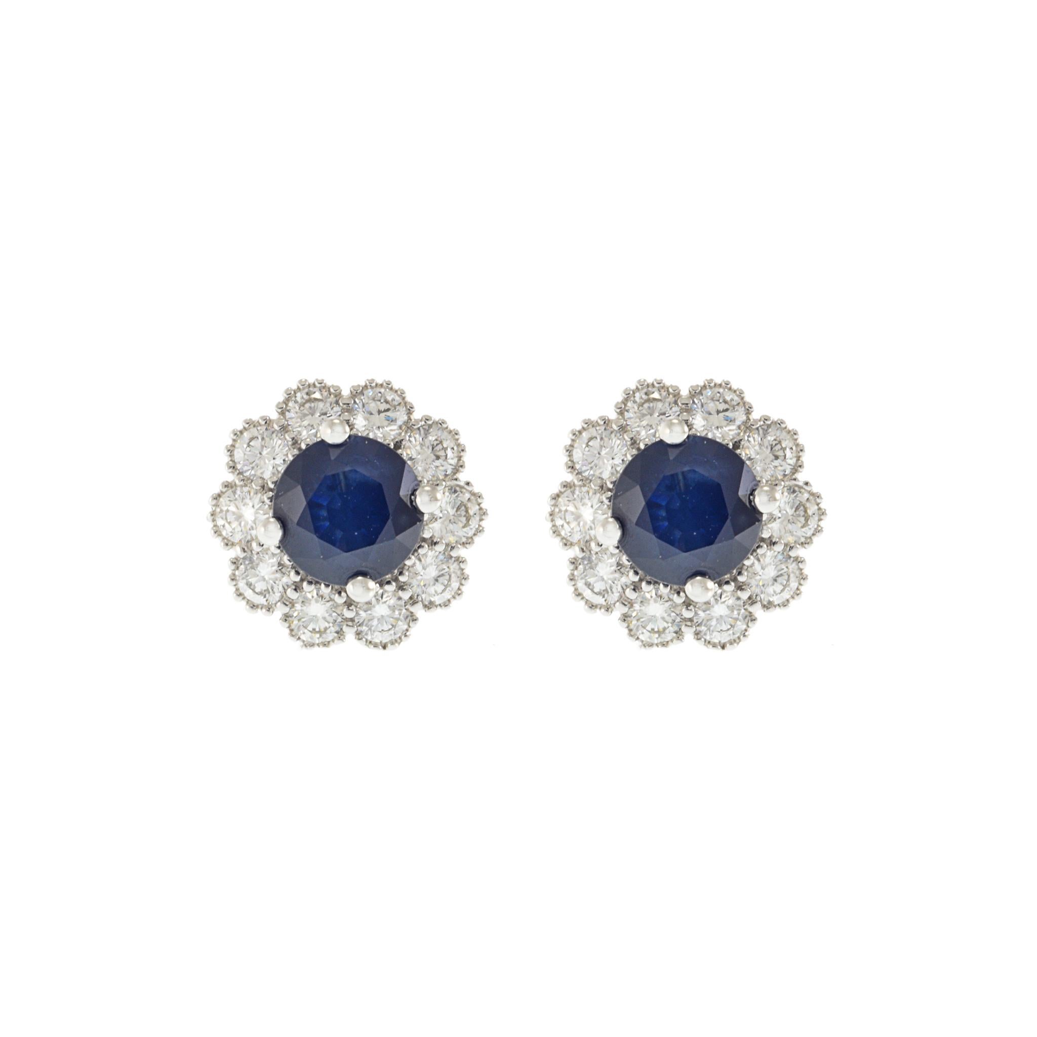 14KT White Gold Halo Earrings with Blue Sapphires Surrounded by Round Cut Diamonds. These elegant earrings feature a total of 2.12 carats of round cut blue sapphires, encircled by 0.88 carats of G-VS round cut diamonds. Crafted from luxurious 14KT