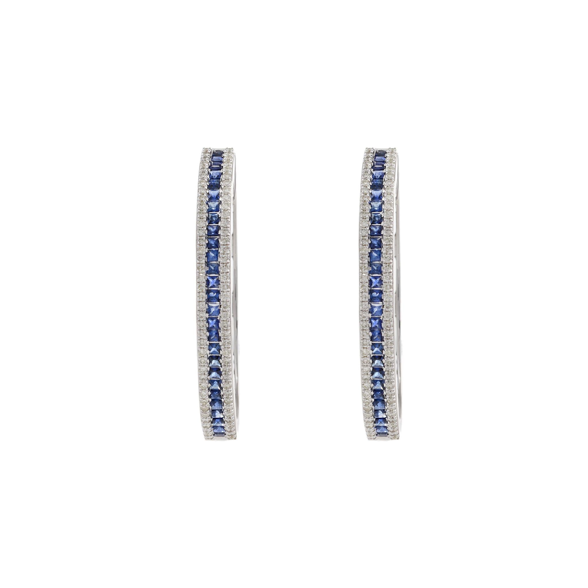 14KT White Gold Oval Hoop Earrings with Round Cut Diamonds and Princess Cut Sapphires. These elegant earrings feature 0.93 carats total weight of round cut diamonds and 2.27 carats total weight of blue princess cut sapphires. The luxurious 14KT