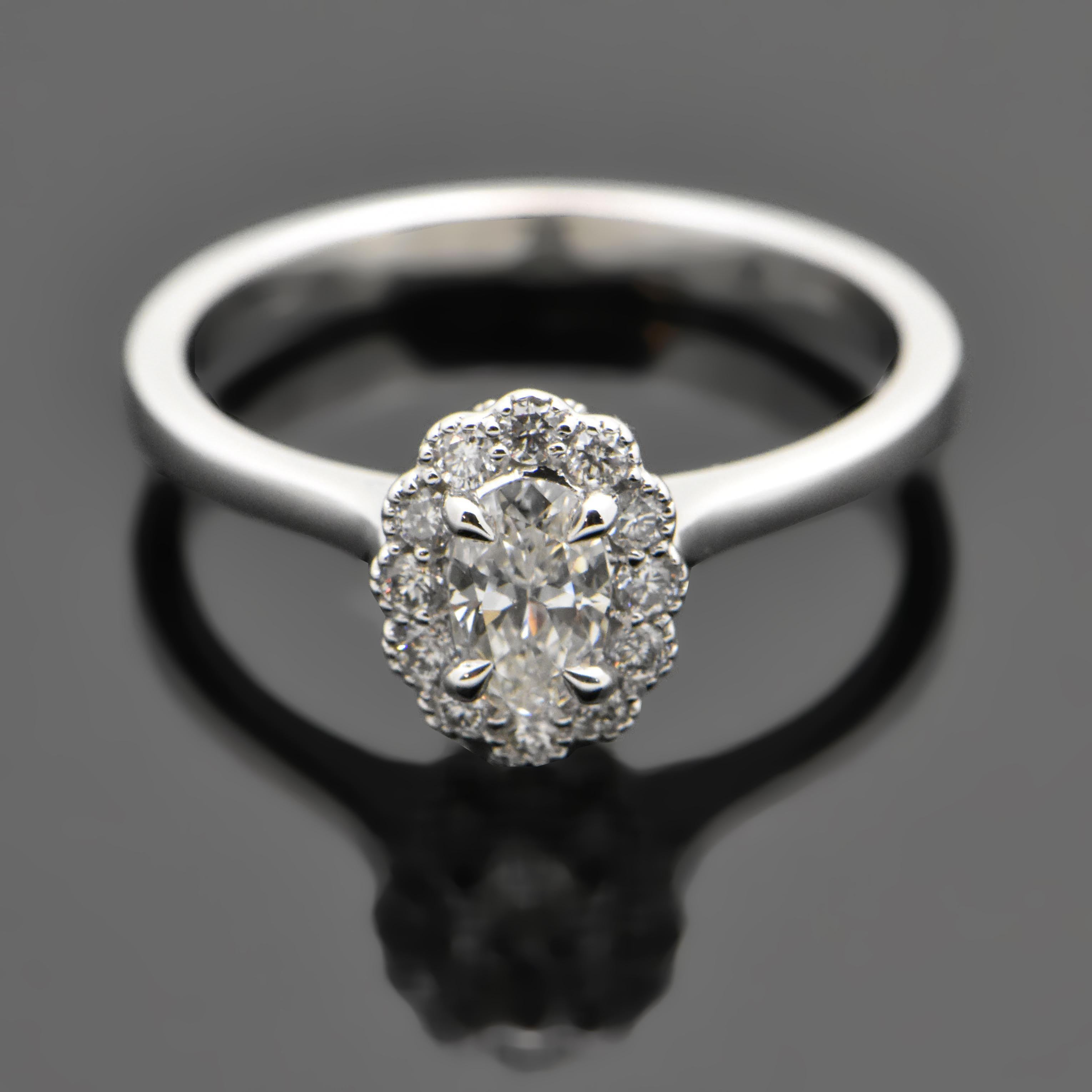 This is a 14kt white gold ring featuring an oval-cut diamond estimated weight of 0.35ct and 4 claw prongs. The center diamond is surrounded by 12 diamonds with an estimated 0.16cttw and file milgrain detail underneath. Estimated weight of gold is