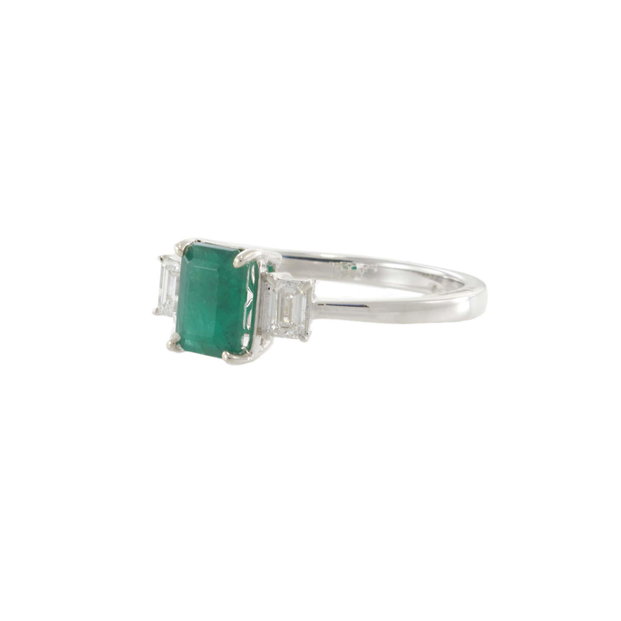 Elegant and timeless, this 14KT white gold three-stone ring features a 1.00-carat emerald-cut emerald at center, flanked by two step-cut diamonds totaling 0.28 carats. The clean symmetry and luminous contrast between the vivid green and white gold