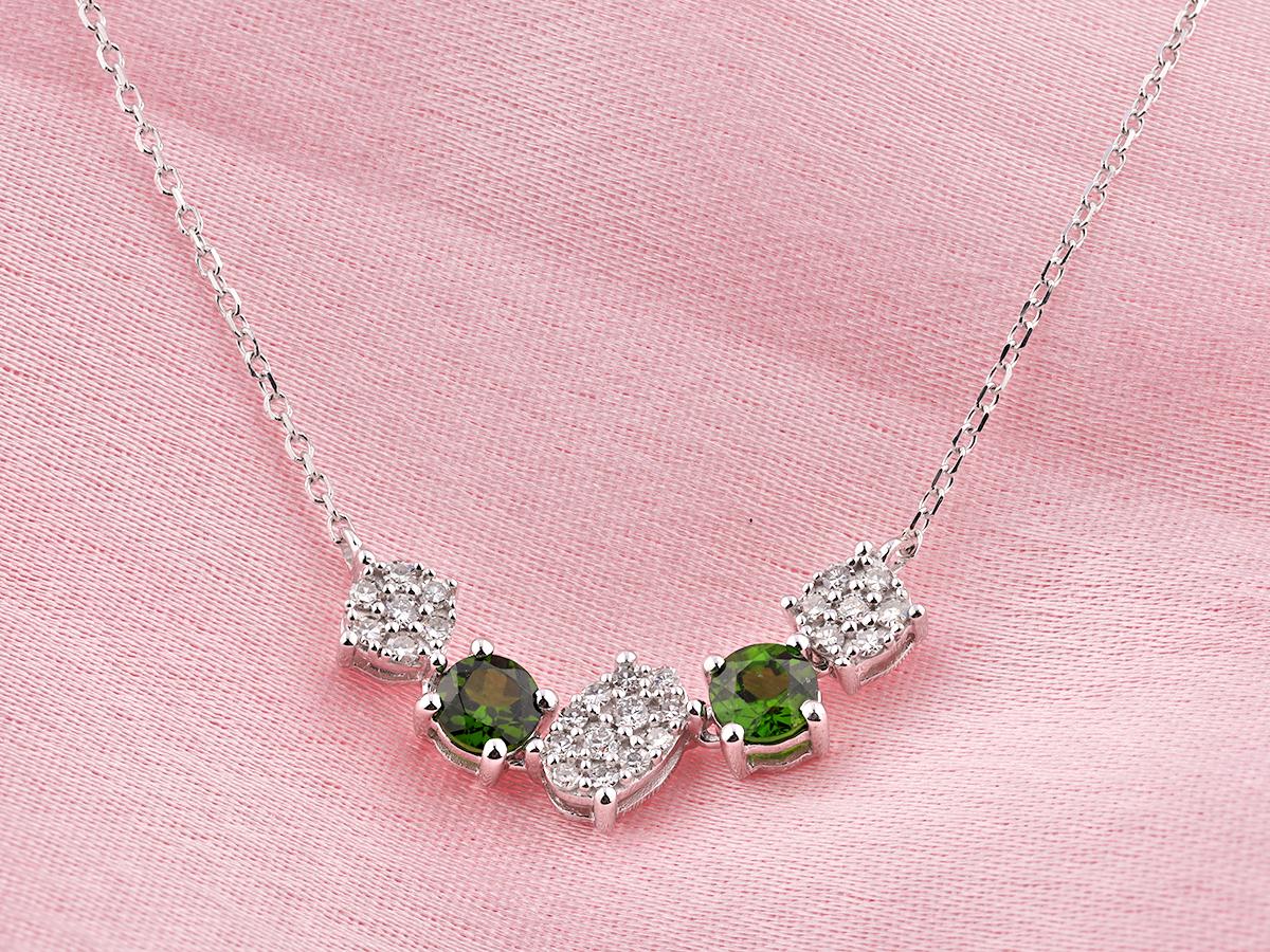 Die Halskette zeichnet sich durch ein elegantes, modernes Design aus, bei dem die Edelsteine in einem sanften Bogen oder einer geschwungenen Stabform angeordnet sind. Das Design wechselt zwischen einzelnen grünen Steinen im Rundschliff und