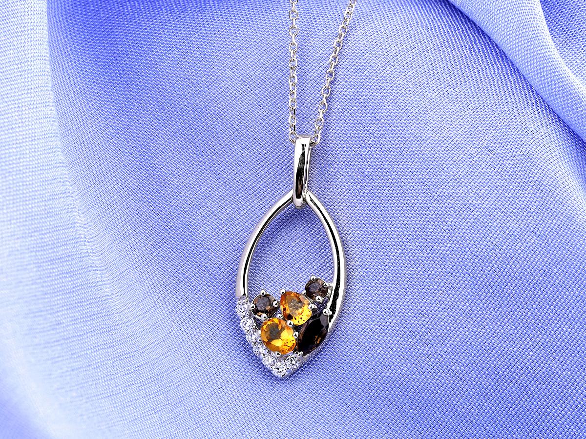 Le pendentif est doté d'une élégante monture ouverte en or blanc de forme marquise ou ovale. À l'intérieur de ce cadre, près du bas, se trouve une charmante grappe de pierres précieuses de différentes couleurs. Le bord inférieur gauche de la monture