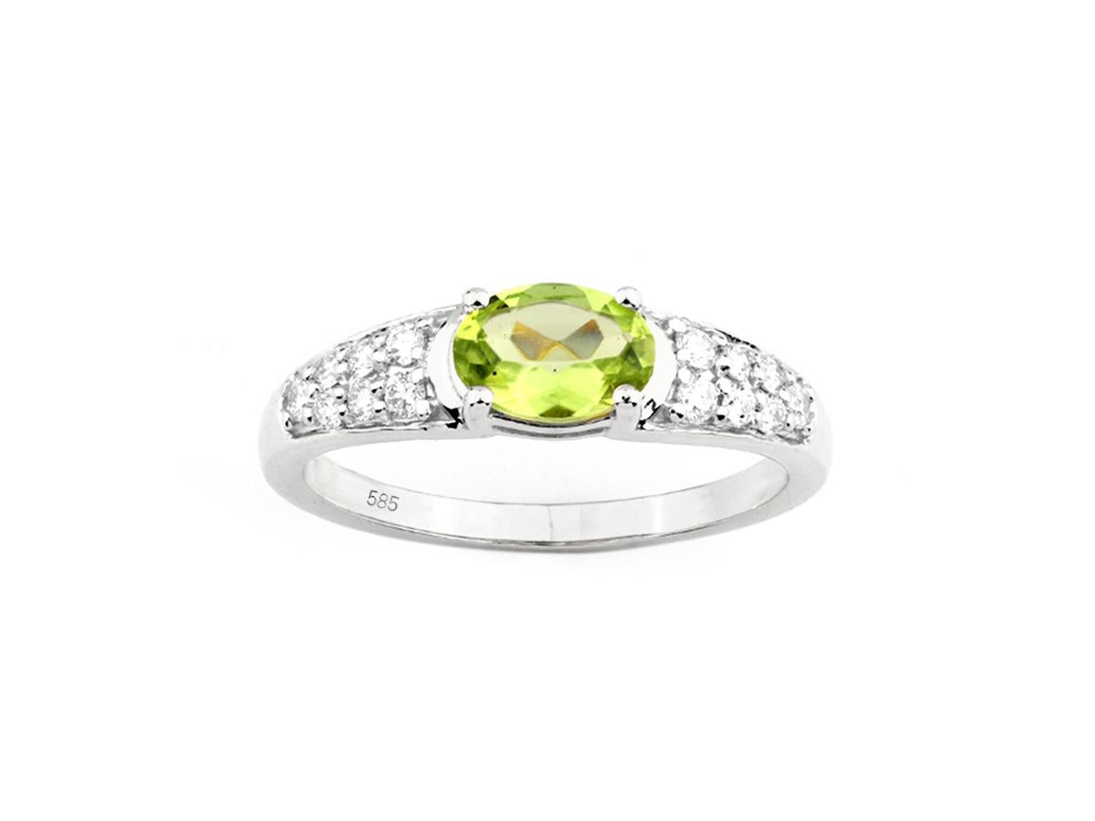 Der Ring hat ein klassisches, elegantes Design. Ein auffälliger Peridot im Ovalschliff ist in der Mitte mit Zacken besetzt. Die Schultern des Bandes sind mit mehreren kleinen, runden weißen Diamanten besetzt, die sich nach unten hin verjüngen und