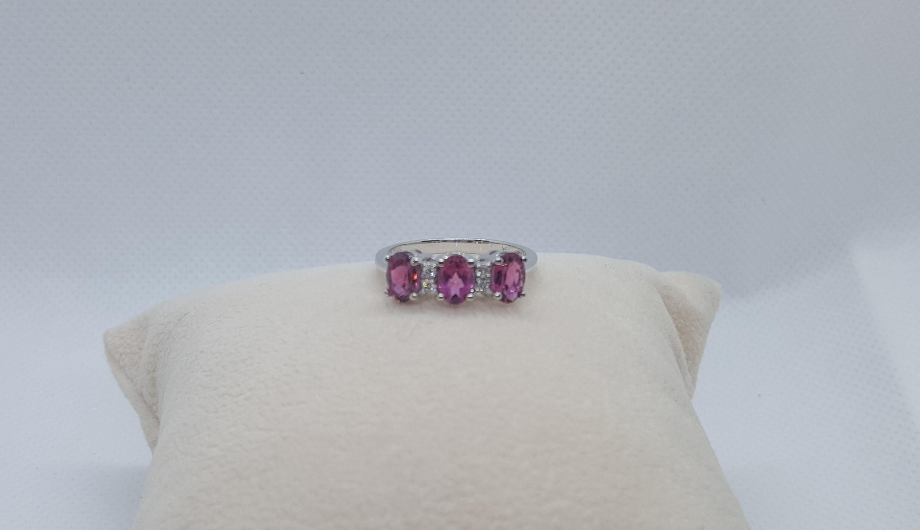 14kt white gold ring with three 6mm x 4mm oval rhodolites and three round brilliant diamonds of .05cttw. The ring is size 7, weighs 3.1 grams, and tapers from 6mm (top) to 2mm (base). The diamonds are well-proportioned, g/h in color and si in