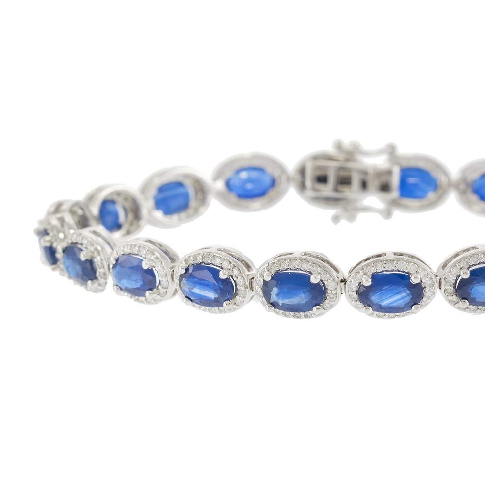 This luxurious bracelet features a seamless row of vivid oval-cut sapphires, each encircled by a delicate halo of round-cut diamonds. Crafted in 14KT white gold, the design blends timeless elegance with bold color. With 12.00 carats of sapphires and