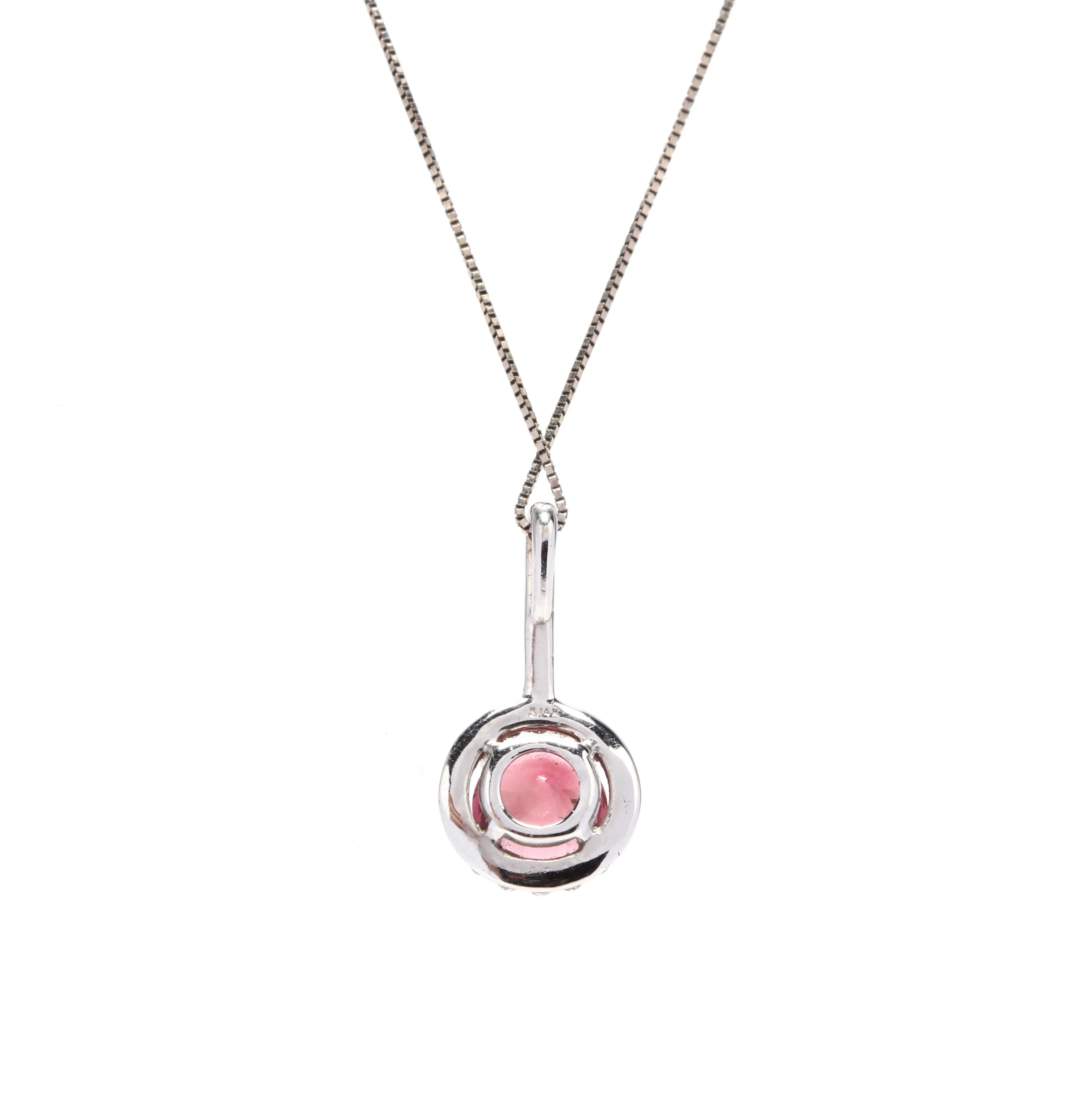 A 14 karat white gold, pink tourmaline, and diamond pendant necklace. A prong set, round cut pink tourmaline surrounded by a halo of round full cut diamonds and with a diamond bail and a thin box chain.

Stones:
- pink tourmaline, 1 stone
- round