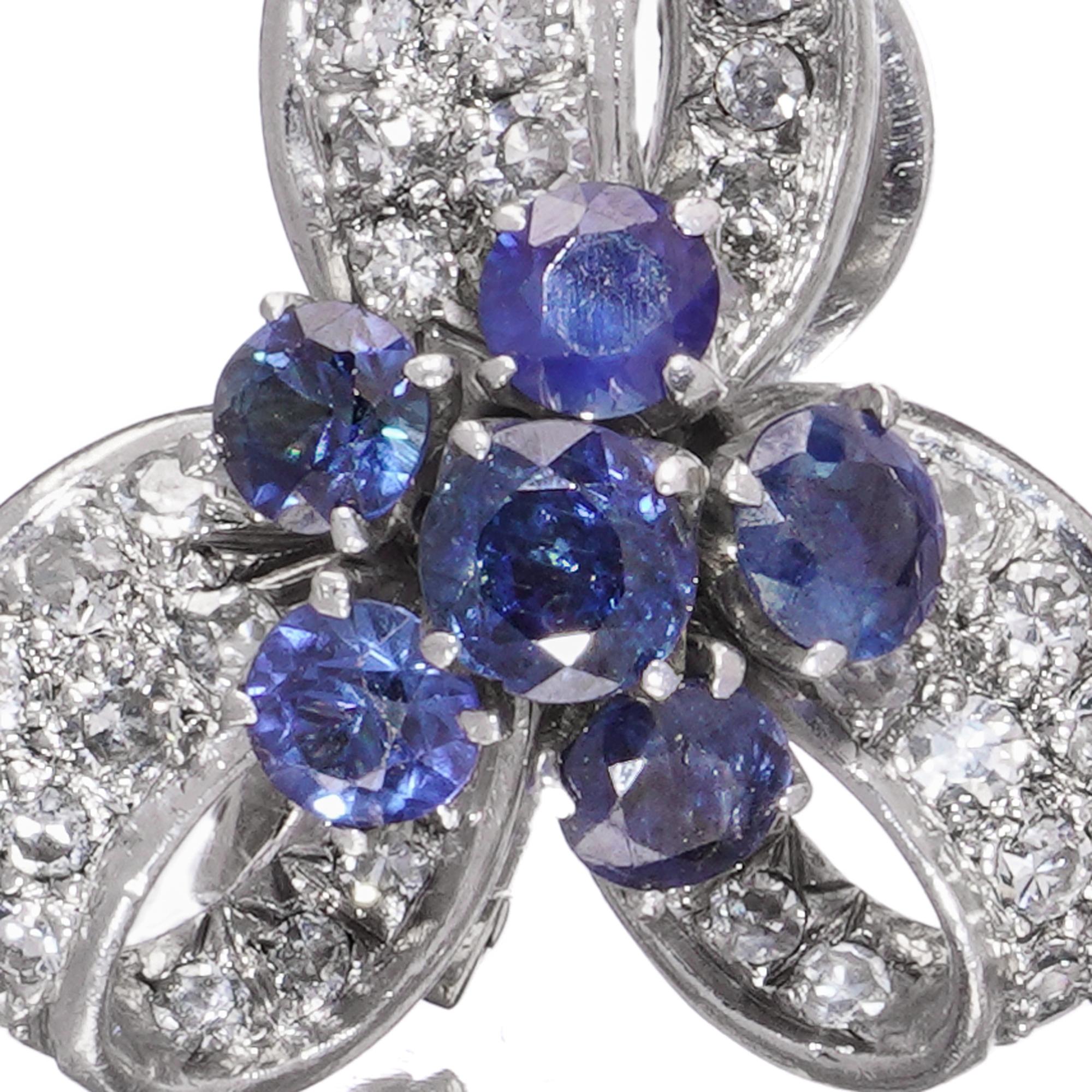 An elegant pair of vintage earrings in 14kt white gold, designed in a stylised ribbon and floral motif. Each earring features a central flower-like cluster of 6 round-cut sapphires, framed by sculptural ribbon loops pavé-set with a total of 48