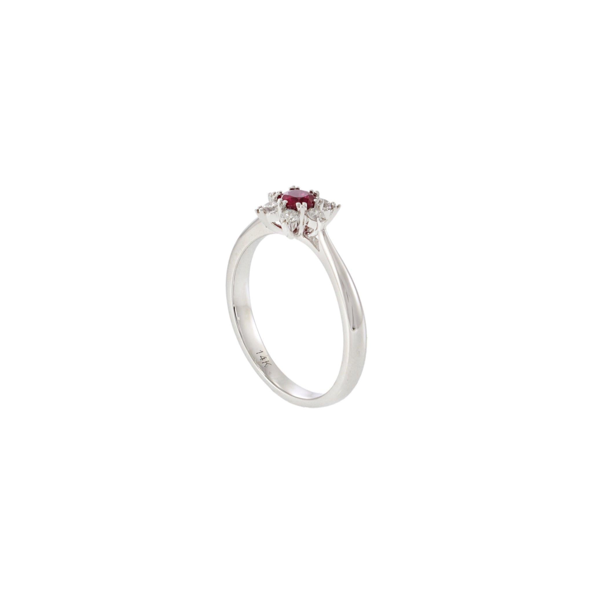 This striking 14KT white gold ring features a vivid 0.36 carat round cut ruby at its center, framed by a sparkling array of round cut diamonds totaling 0.18 carats, arranged in a radiant starburst pattern. The dynamic design and contrast between the