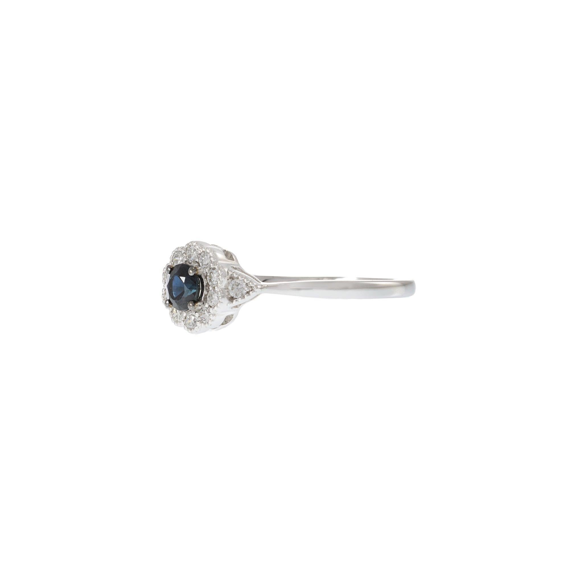 Elegantly crafted in 14KT white gold, this beautiful ring features a captivating flower design, centered with a vibrant 0.26 carat round cut sapphire, surrounded by a shimmering halo of round cut diamonds totaling 0.20 carats. The delicate yet