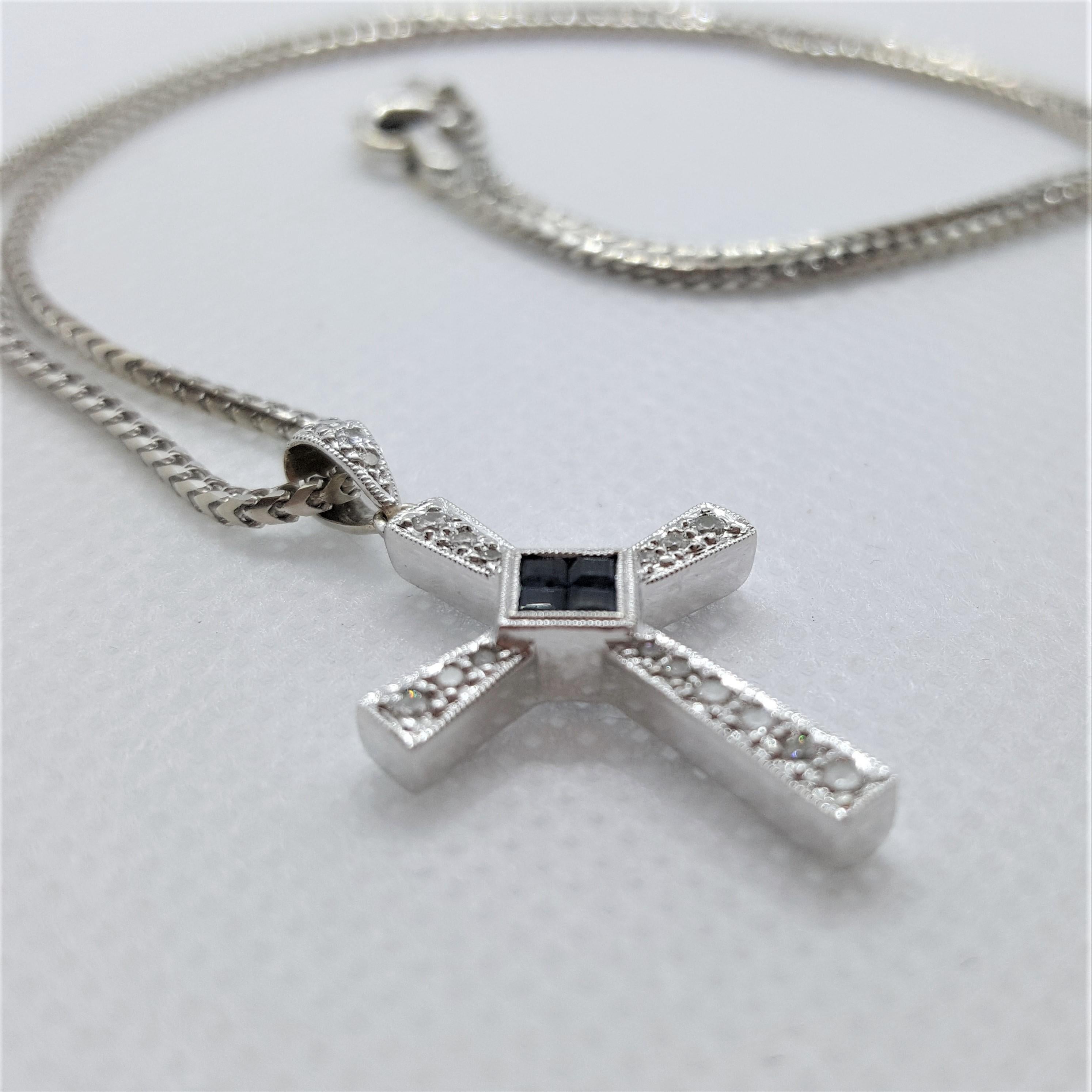 A beautiful 14kt white gold cross with 4 invisible set princess cut blue sapphires of approximately .15cttw, 18 round brilliant diamonds of approximately .25cttw.  The cross is 30mm x 18mm x 3.5mm in size, has a fine multigrain-edging, stamped 585,